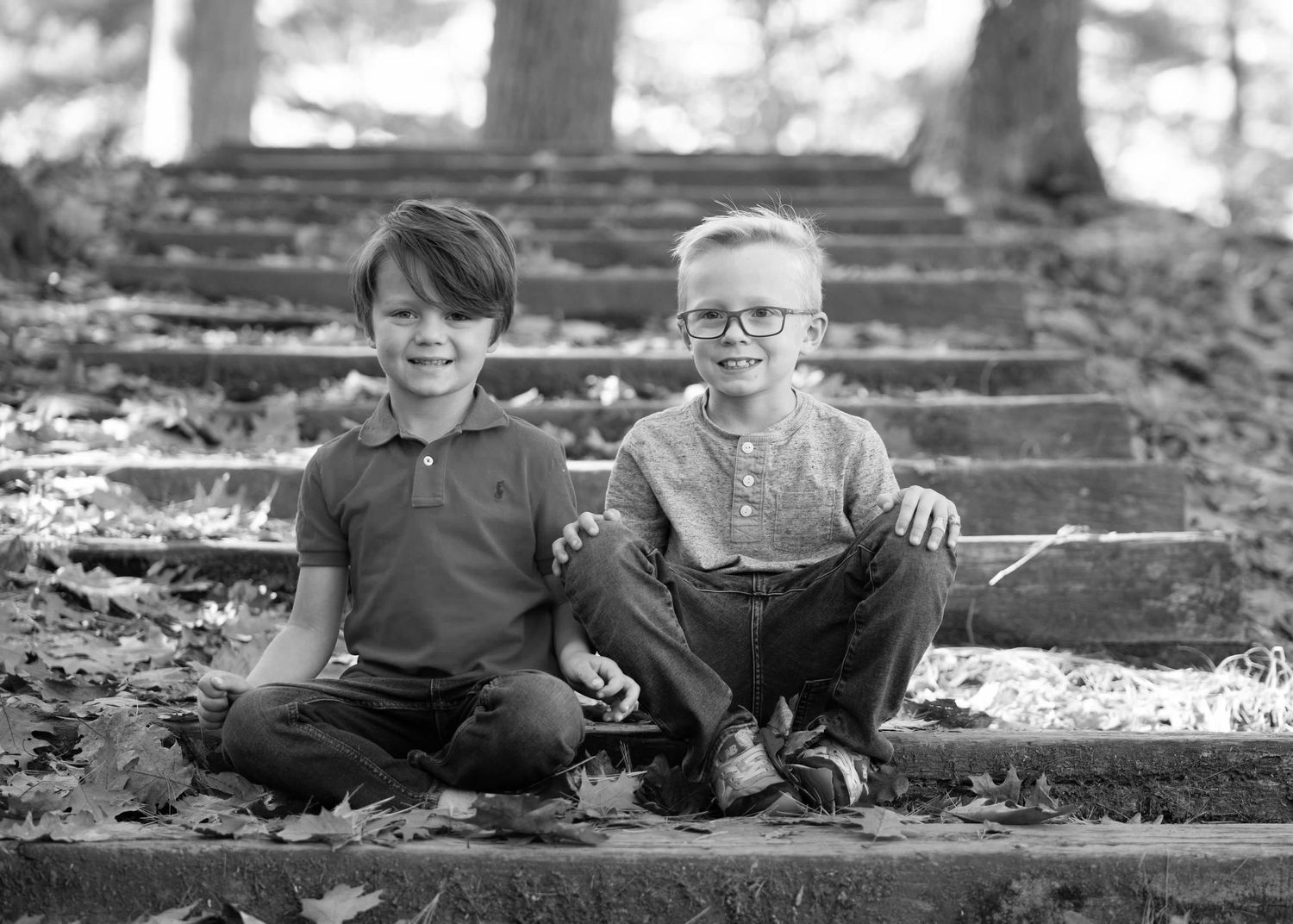 Two boys sit casually together on outdoor wooden steps in black and white photo.