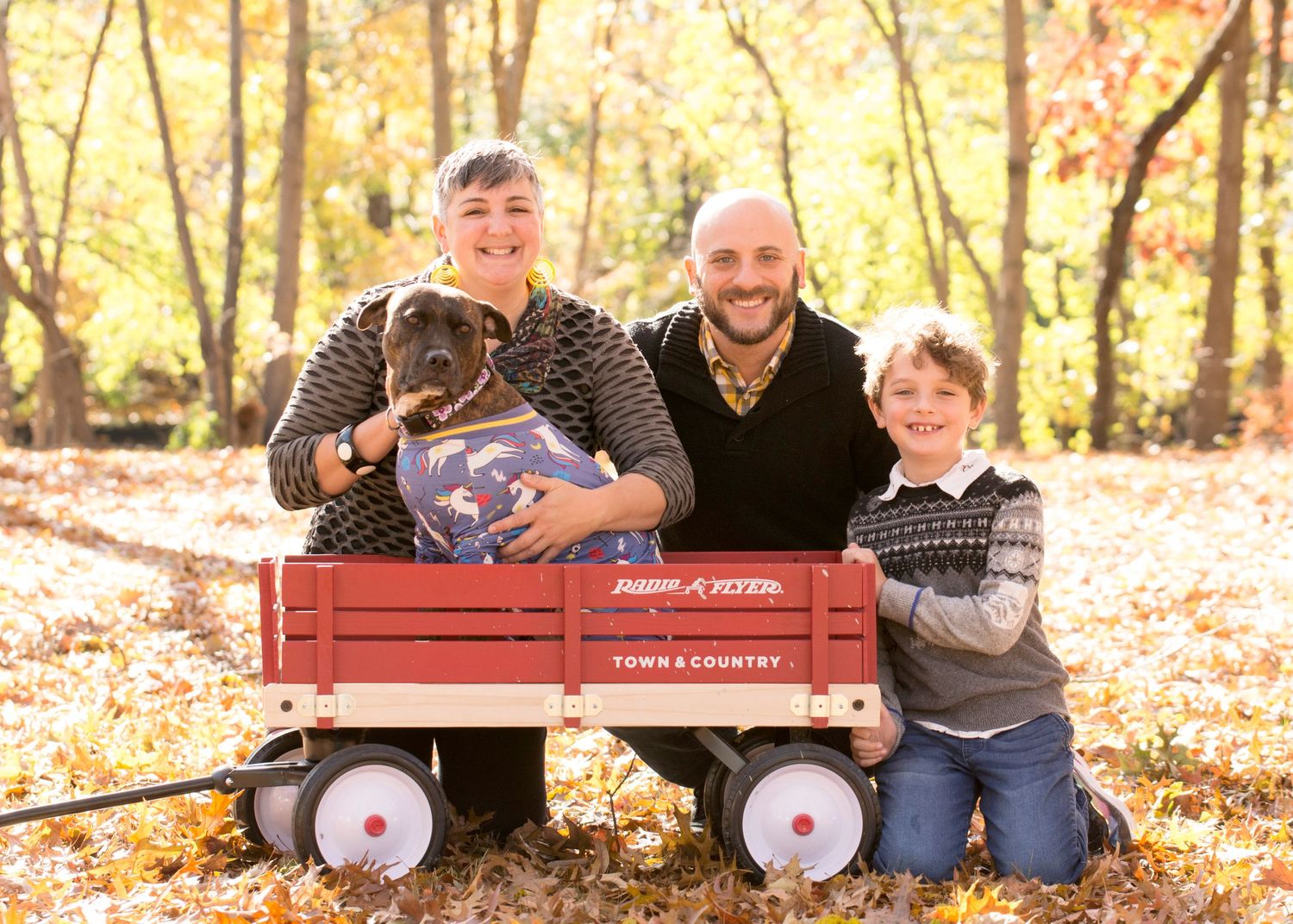 Family with dog poses in red wagon during autumn photoshoot.