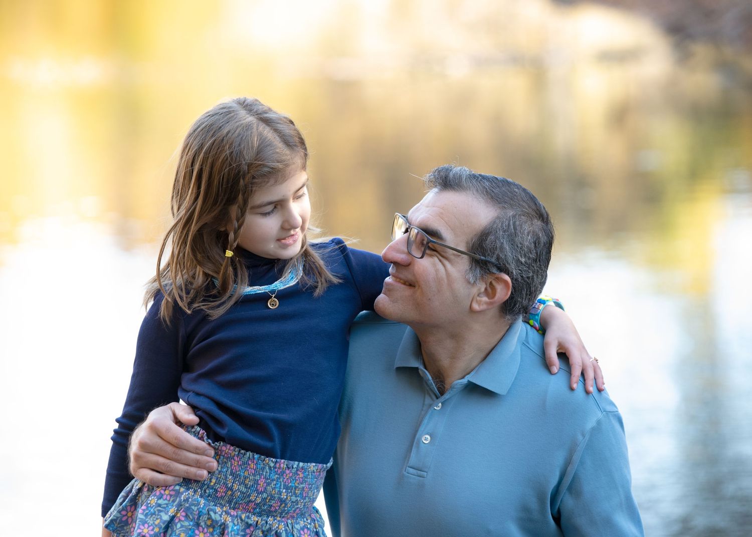 Tender outdoor portrait of an adult and child together by a lake in soft golden light.