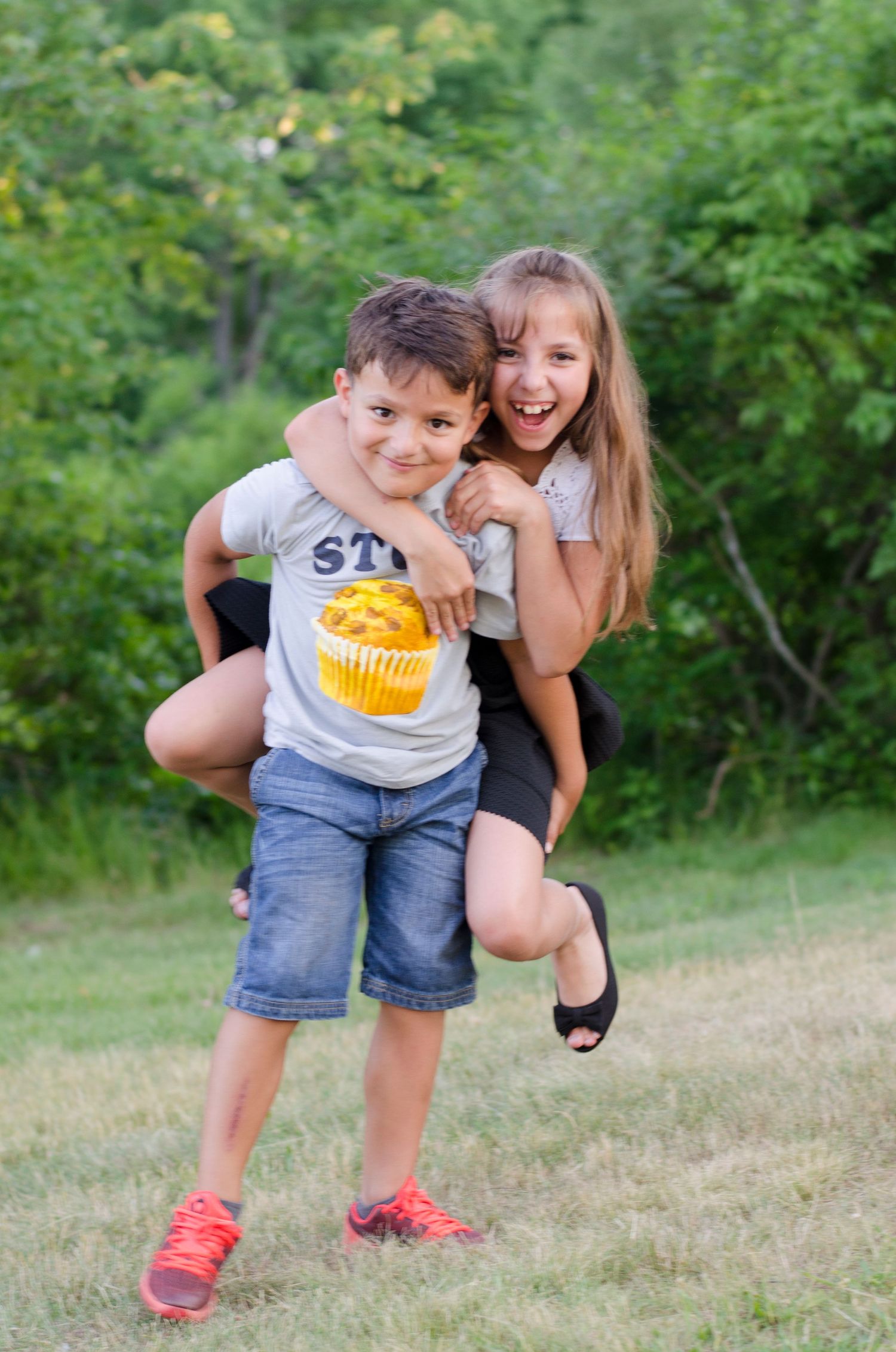 Two playful figures sharing a joyful moment outdoors with one wearing a t-shirt with cupcake design.