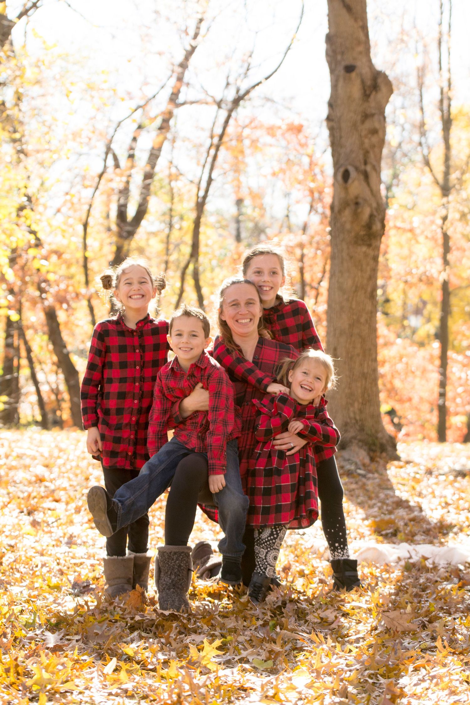 Family of four wearing matching red plaid shirts posing together in autumn forest setting.
