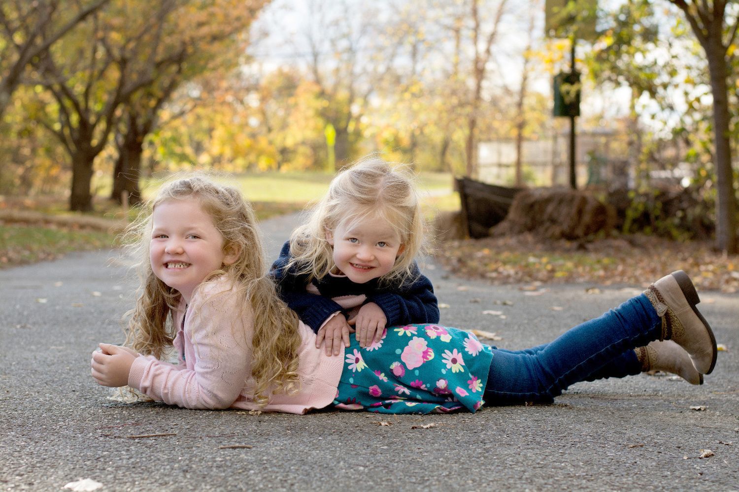 Two children playing and laughing while lying on a path during autumn.
