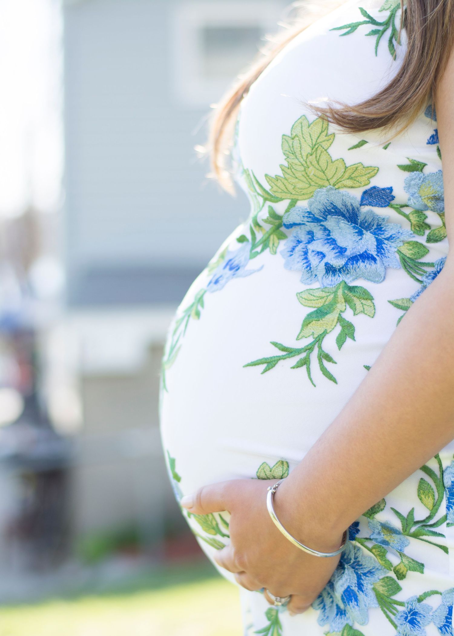 Close up of pregnant belly in blue floral dress outdoors.