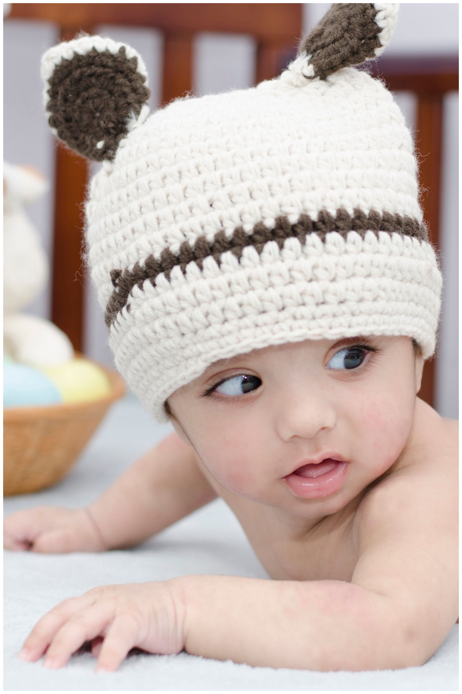 Baby wearing cute white knitted hat with ears lying on soft blanket.