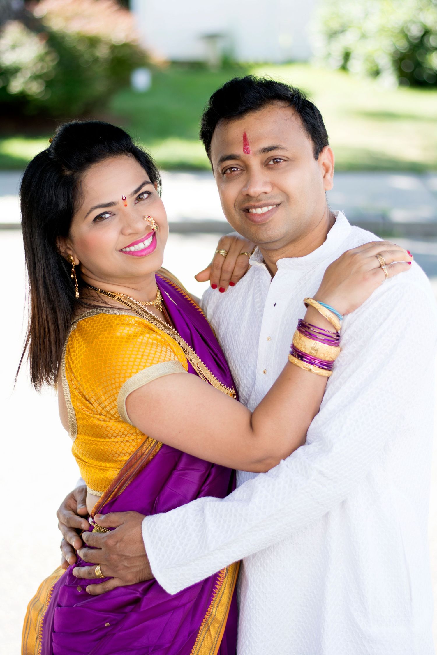 A couple in traditional Indian attire poses together, the woman in yellow and purple sari with colorful bangles.