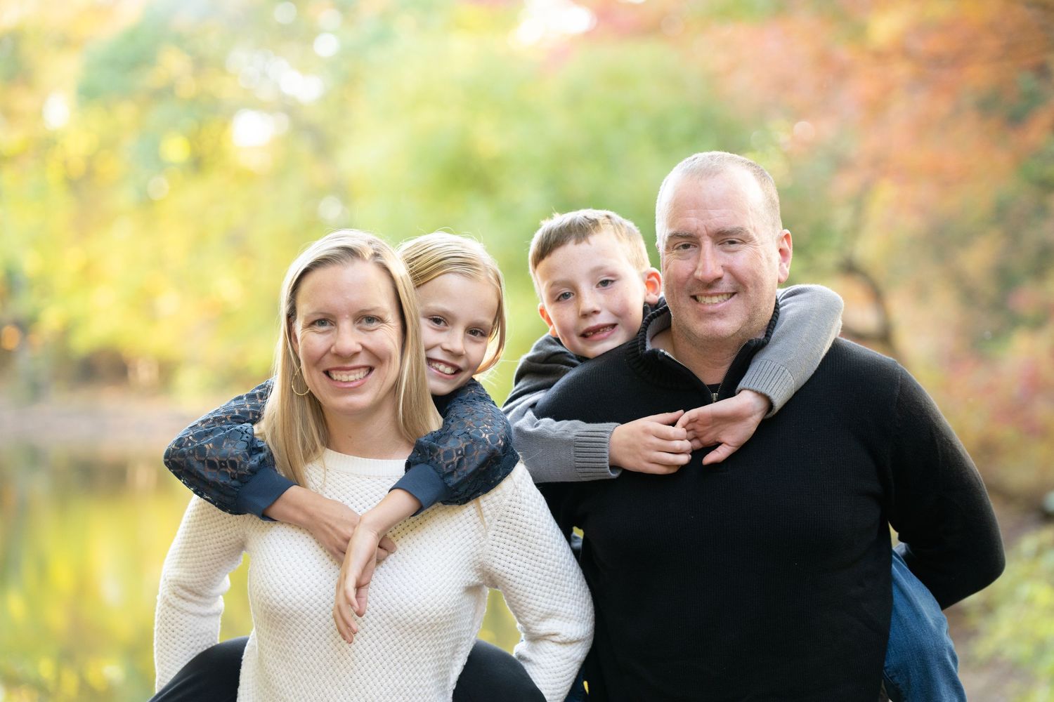 A happy family enjoying an outdoor autumn photoshoot with fall foliage in the background.