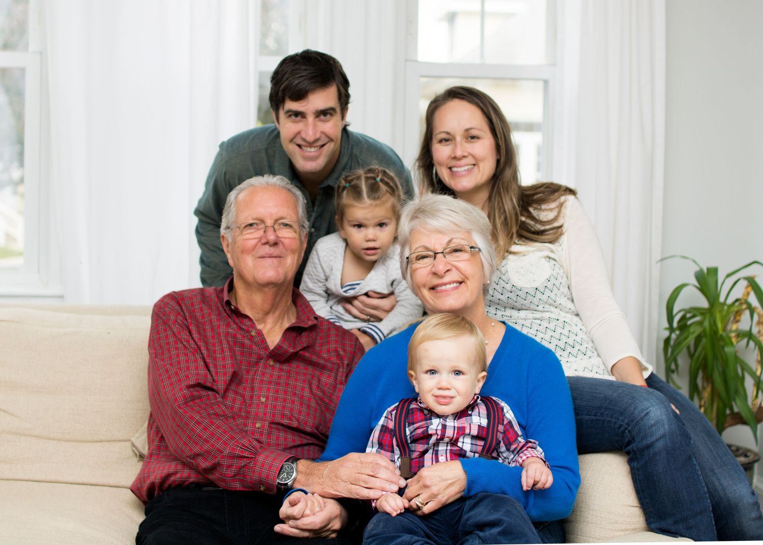 Three generations gather together on a cozy white couch in a bright living room.