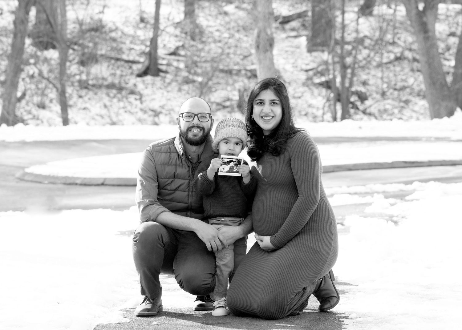 Family of three poses together for black and white winter portrait outdoors.