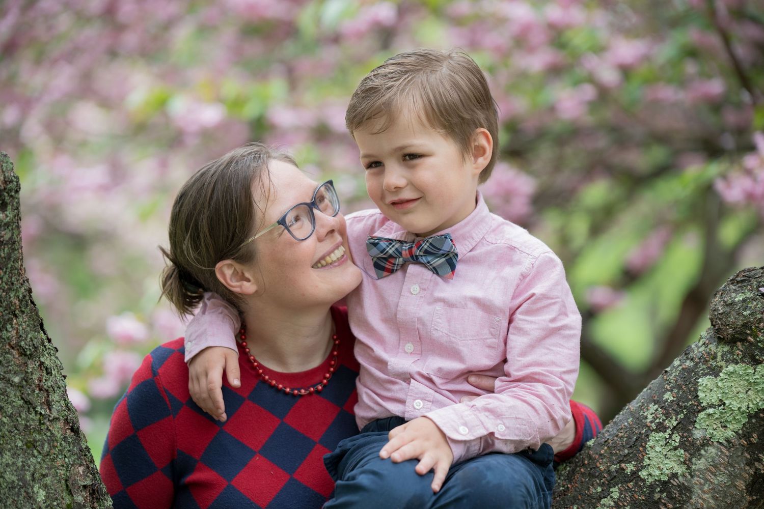 Two people share a tender moment while sitting together among pink cherry blossoms in a spring garden.