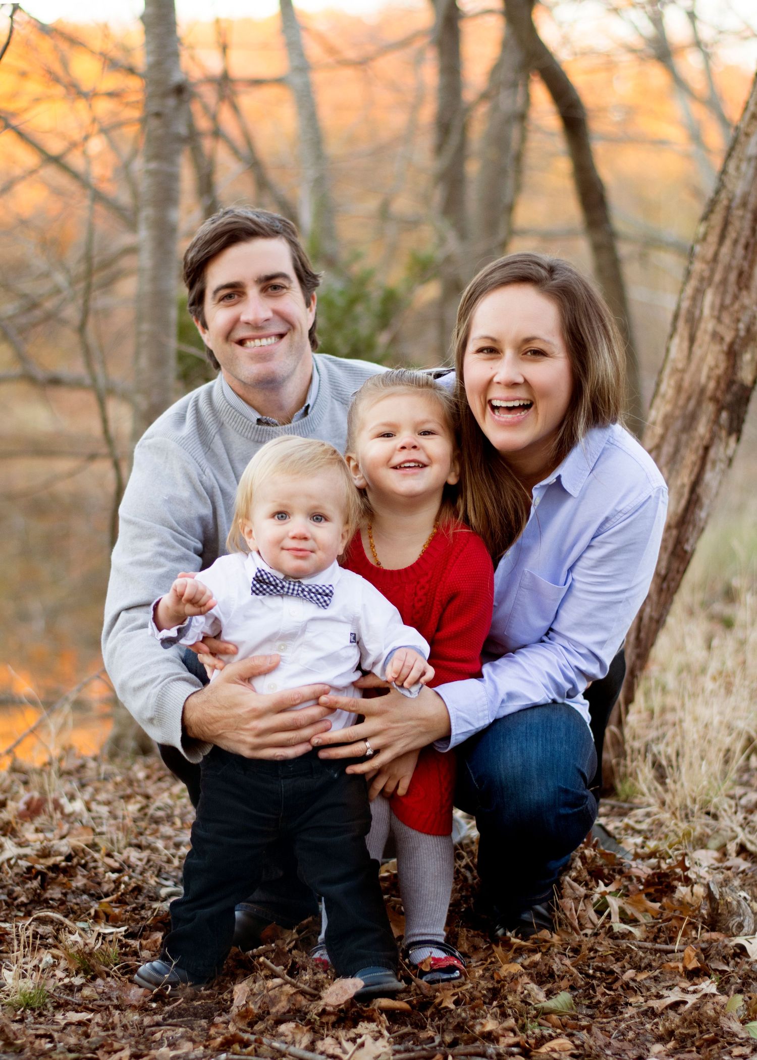 A family group poses together for a casual autumn portrait among fallen leaves.