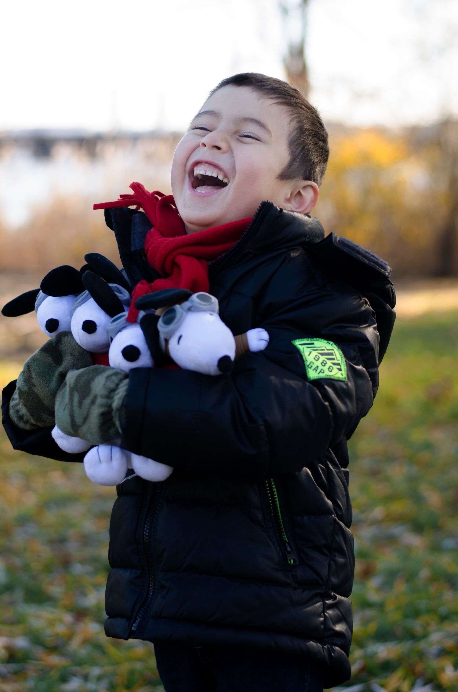 Child laughing while holding stuffed animal toys wearing winter coat outdoors.