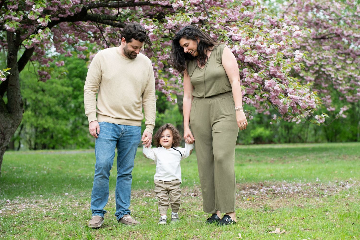 A family enjoys a spring day together under blooming cherry trees in a lush green park setting.