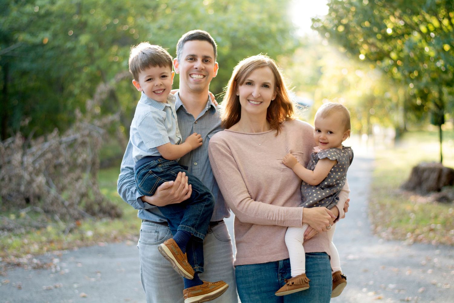 Young family of four posing together on autumn path holding their children.