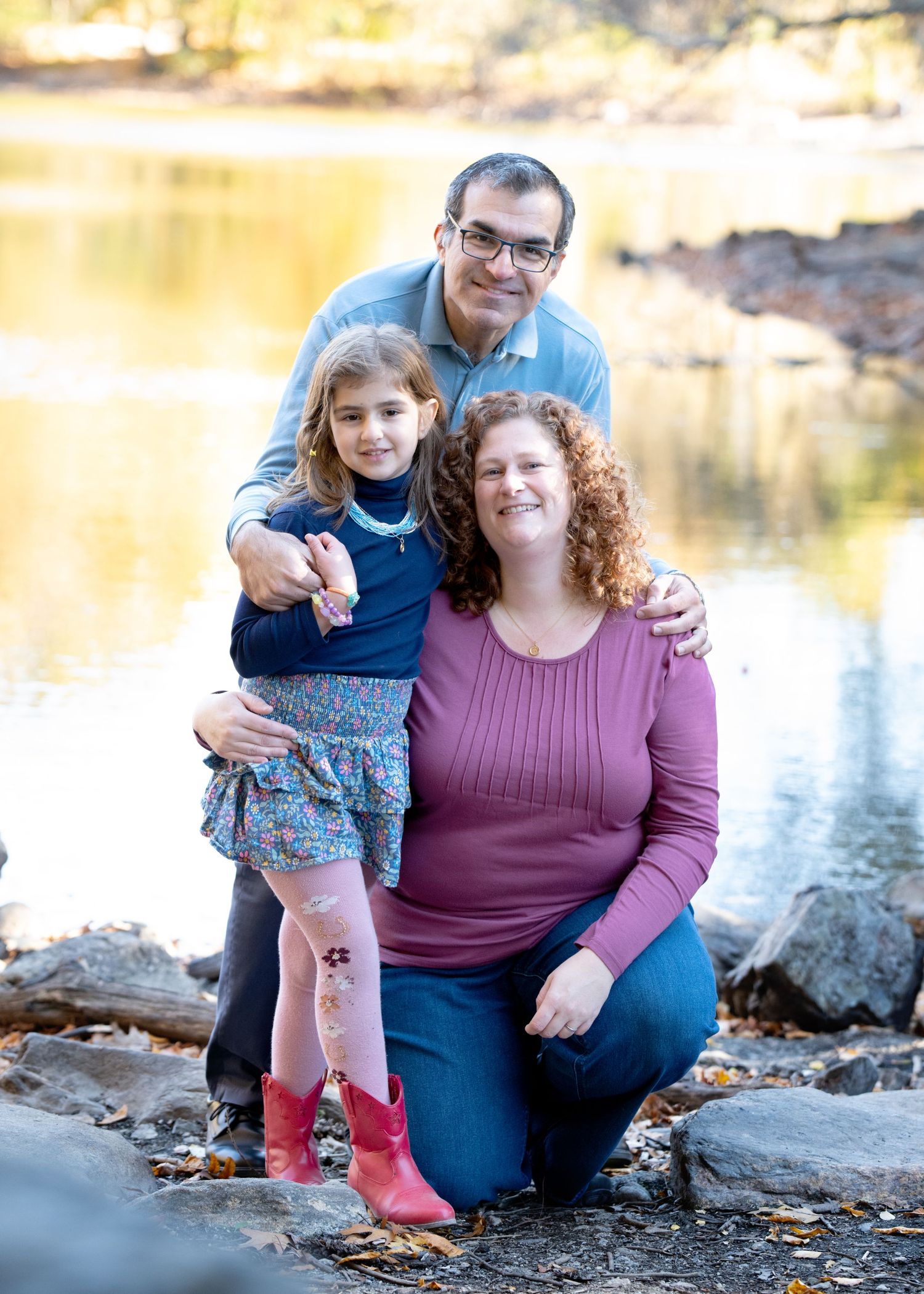 Family portrait by lake with golden autumn reflections in water.