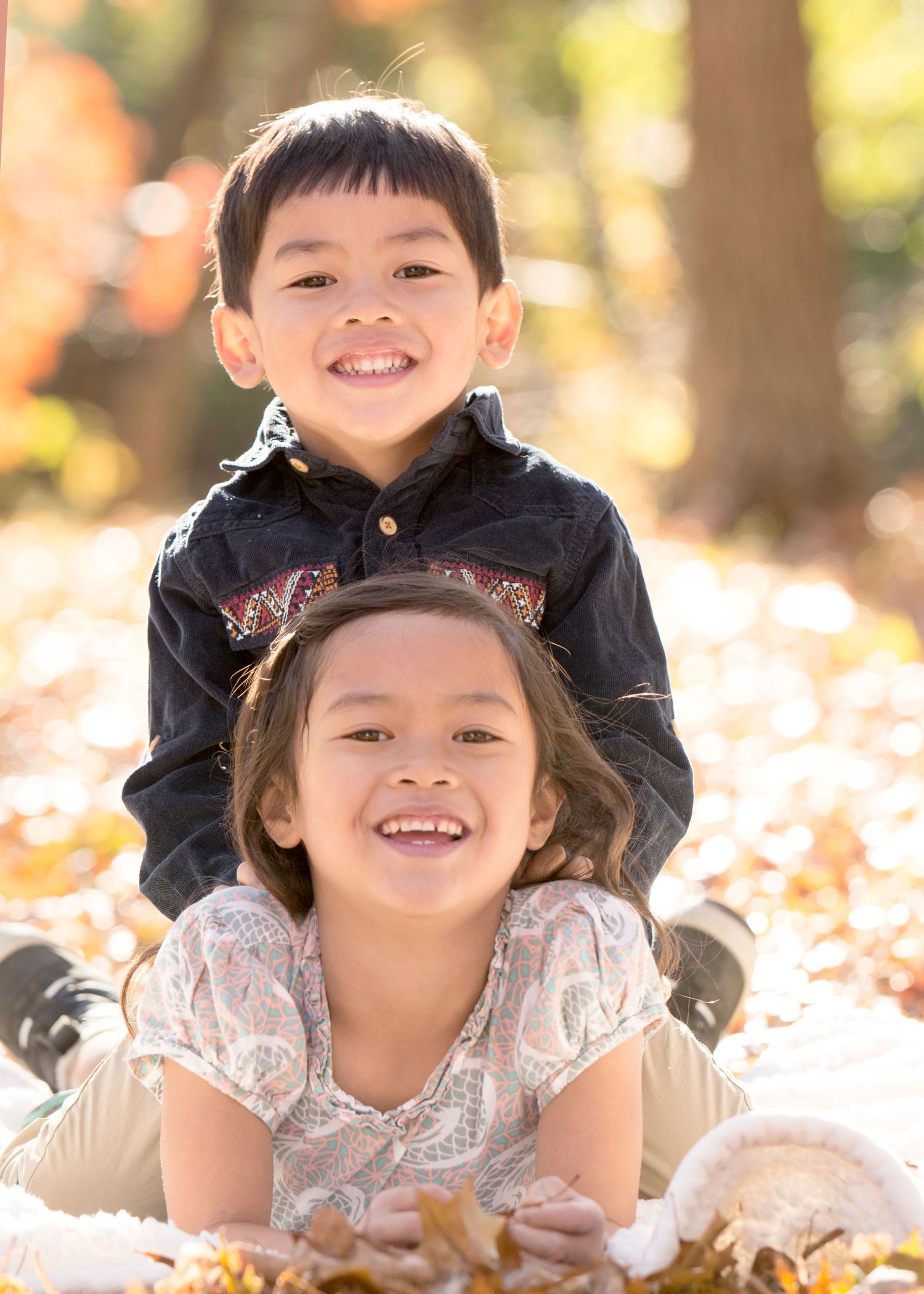 Two children posing playfully among autumn leaves on the ground.
