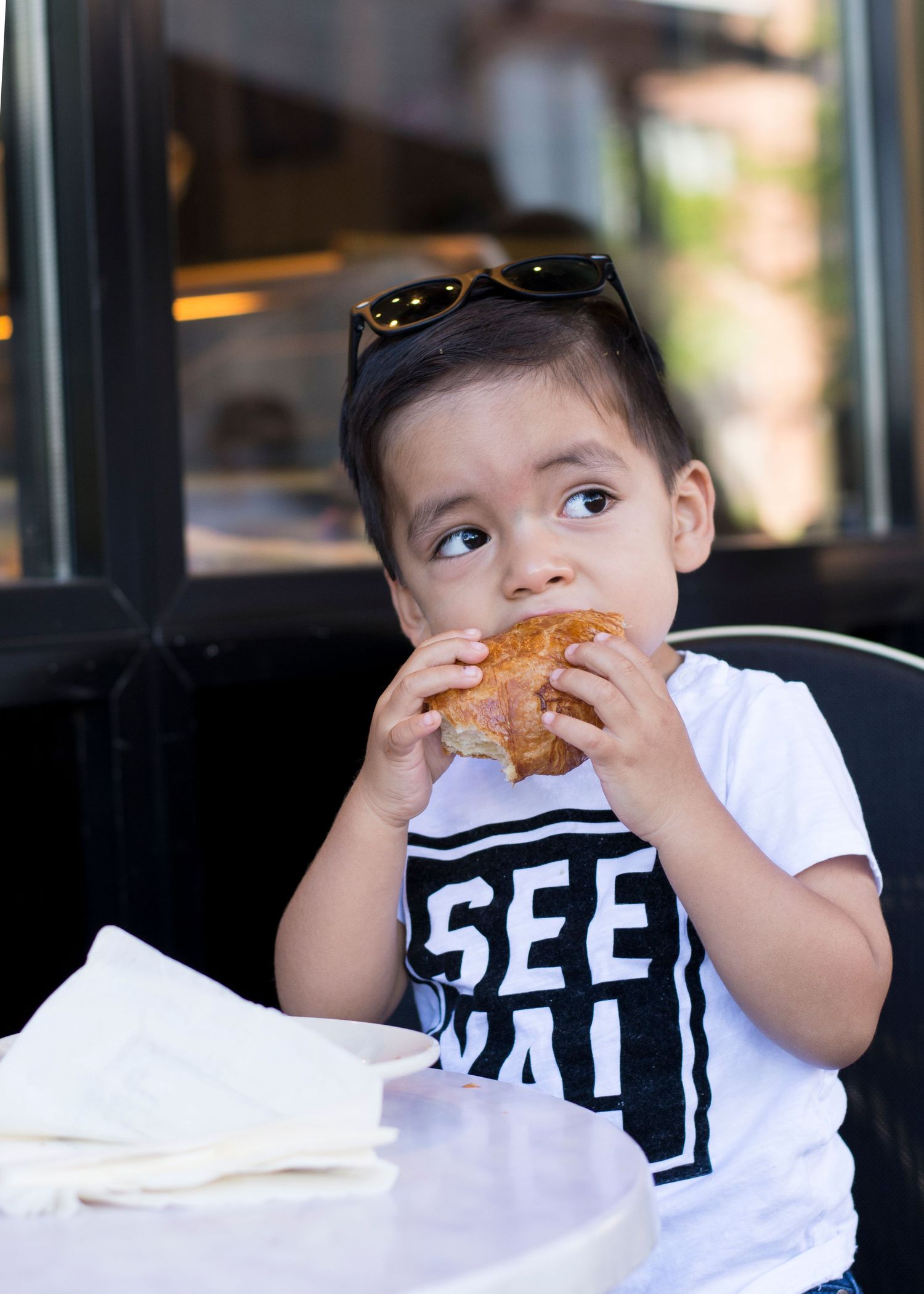 Young child eating sandwich while wearing BFF AT shirt in restaurant setting.