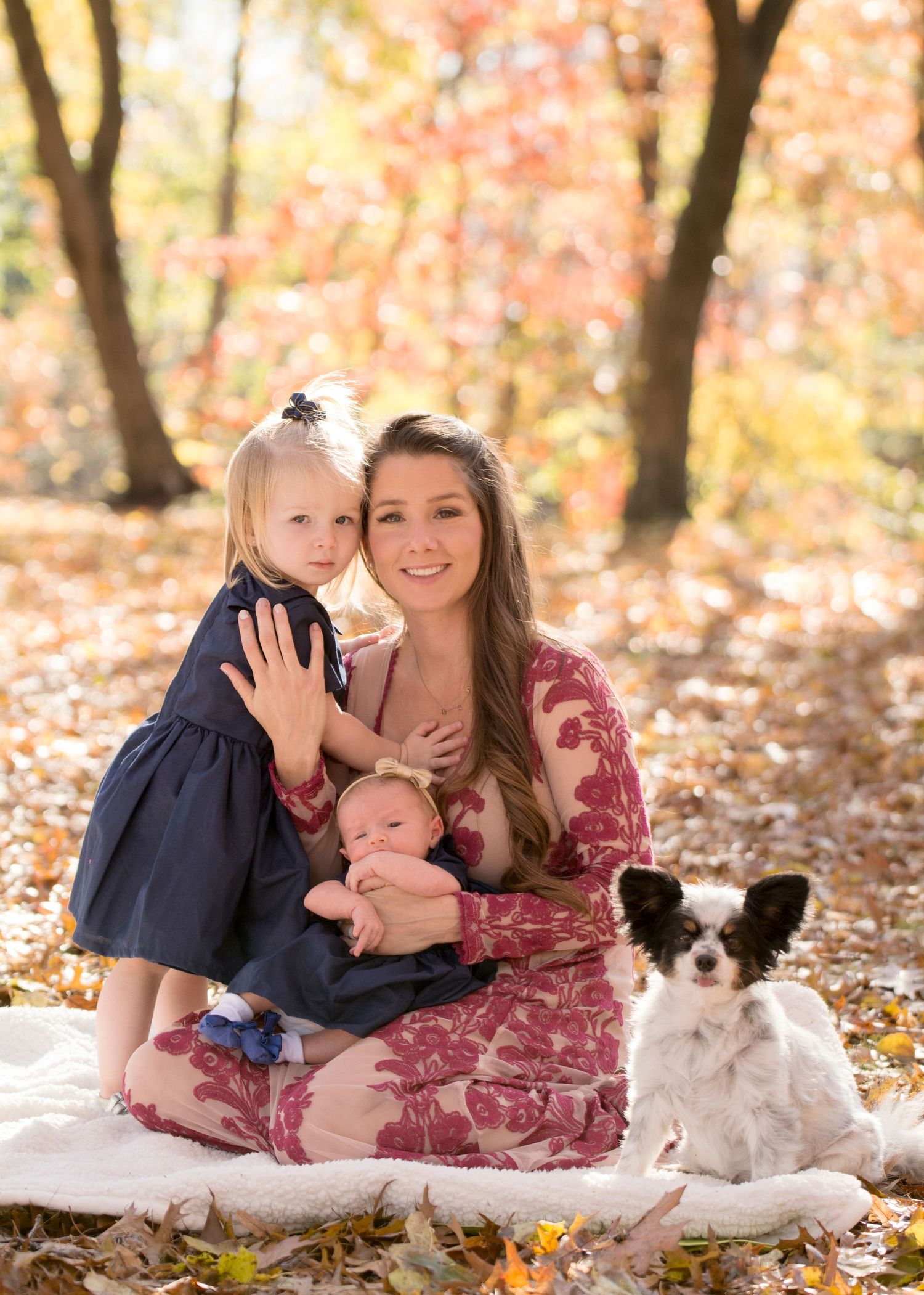 Family portrait on blanket in autumn forest with small dog and baby.