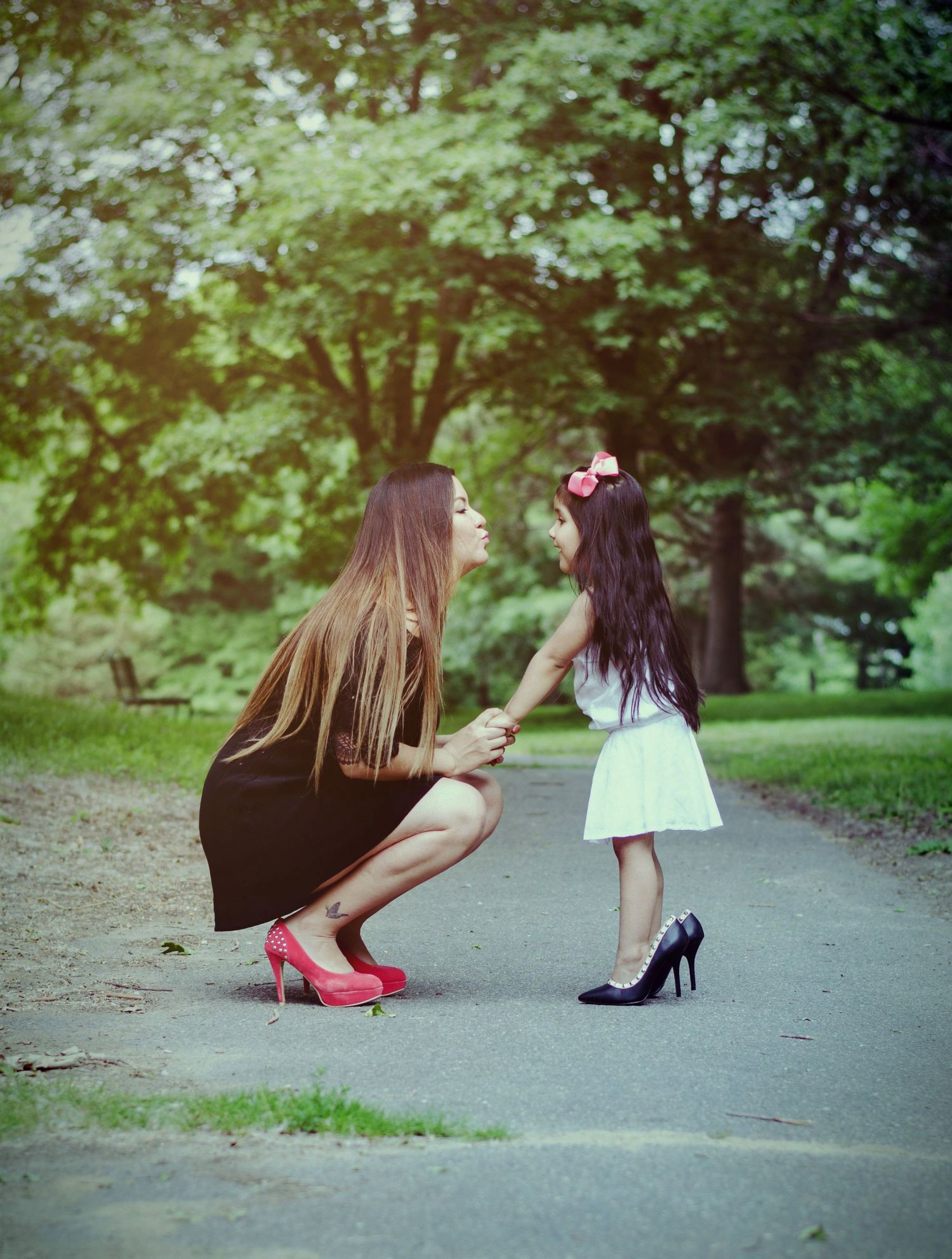 Two people in dresses and heels share a tender moment on a park path.