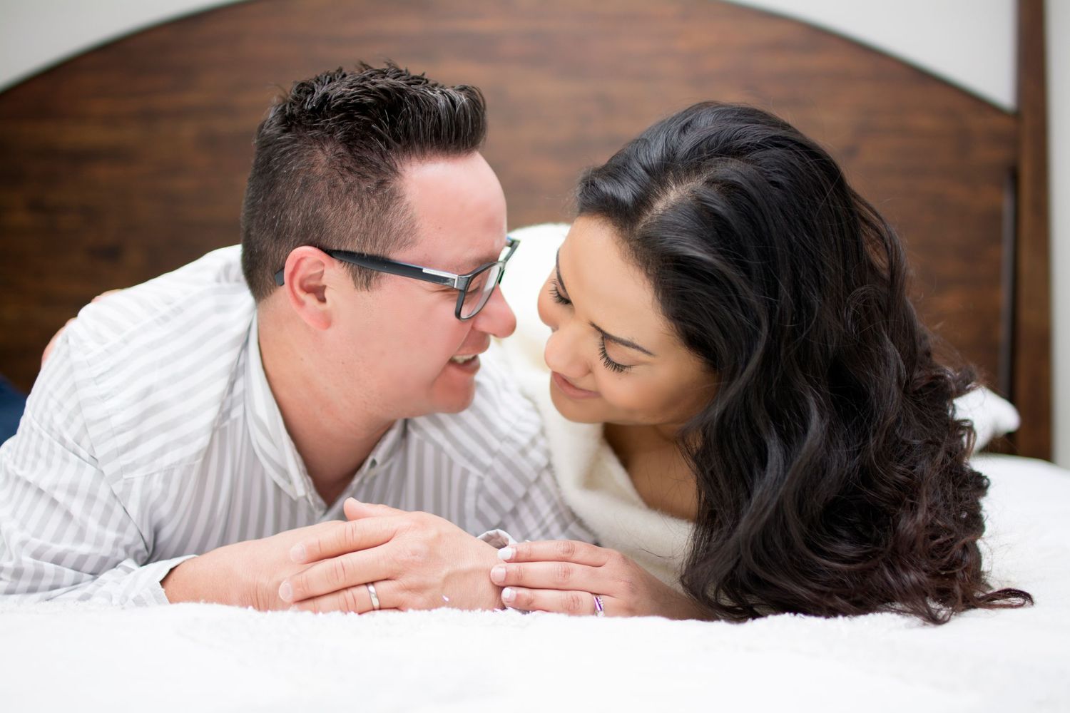 Intimate close-up of couple lying face to face on white bedding.