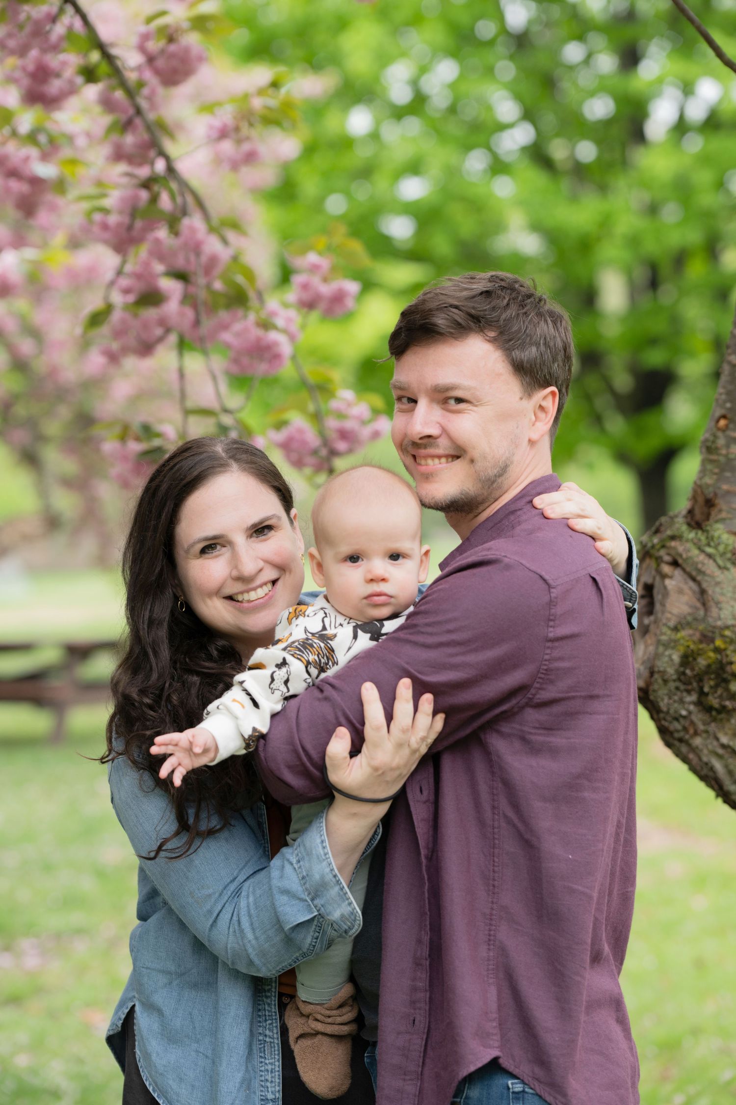 A happy family poses together outdoors under blooming cherry blossoms on a spring day.