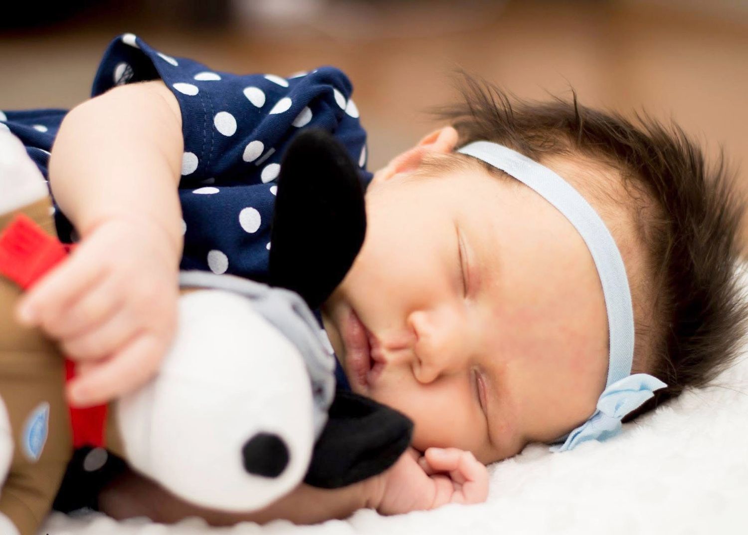 Sleeping baby in polka dot outfit cuddles with plush toy.