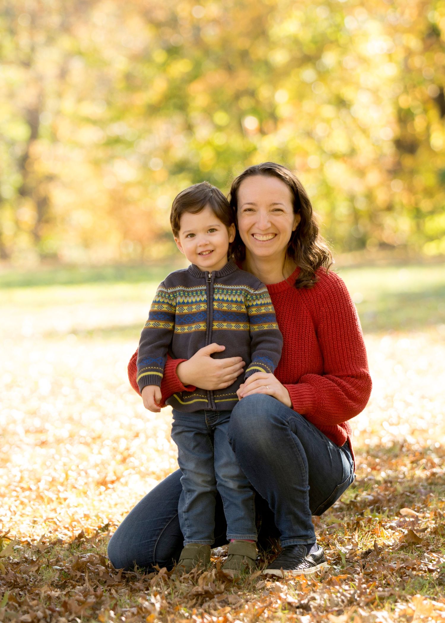 Parent and child posing together on fallen autumn leaves wearing cozy sweaters.
