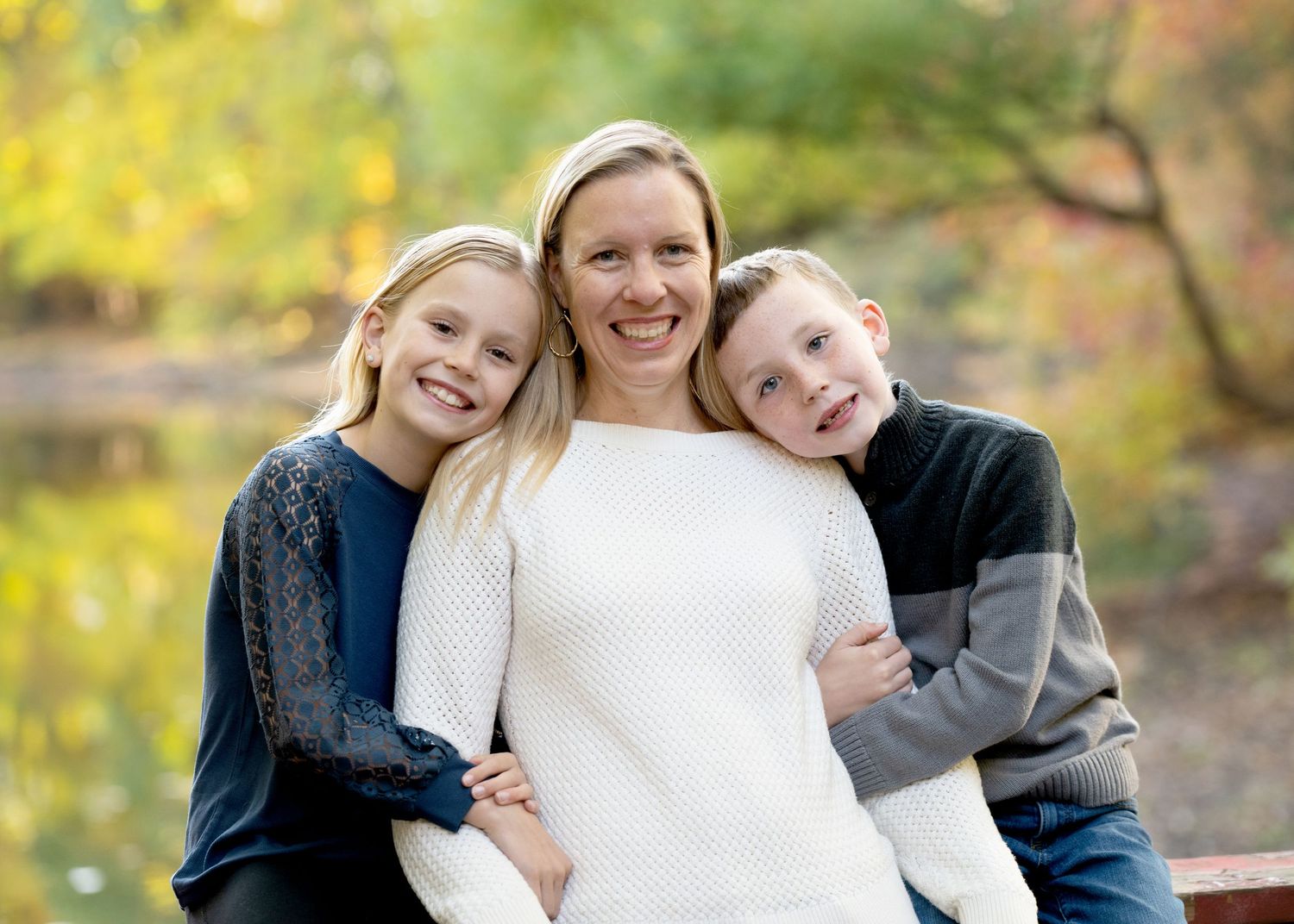 Parent poses with children against blurred yellow autumn background.