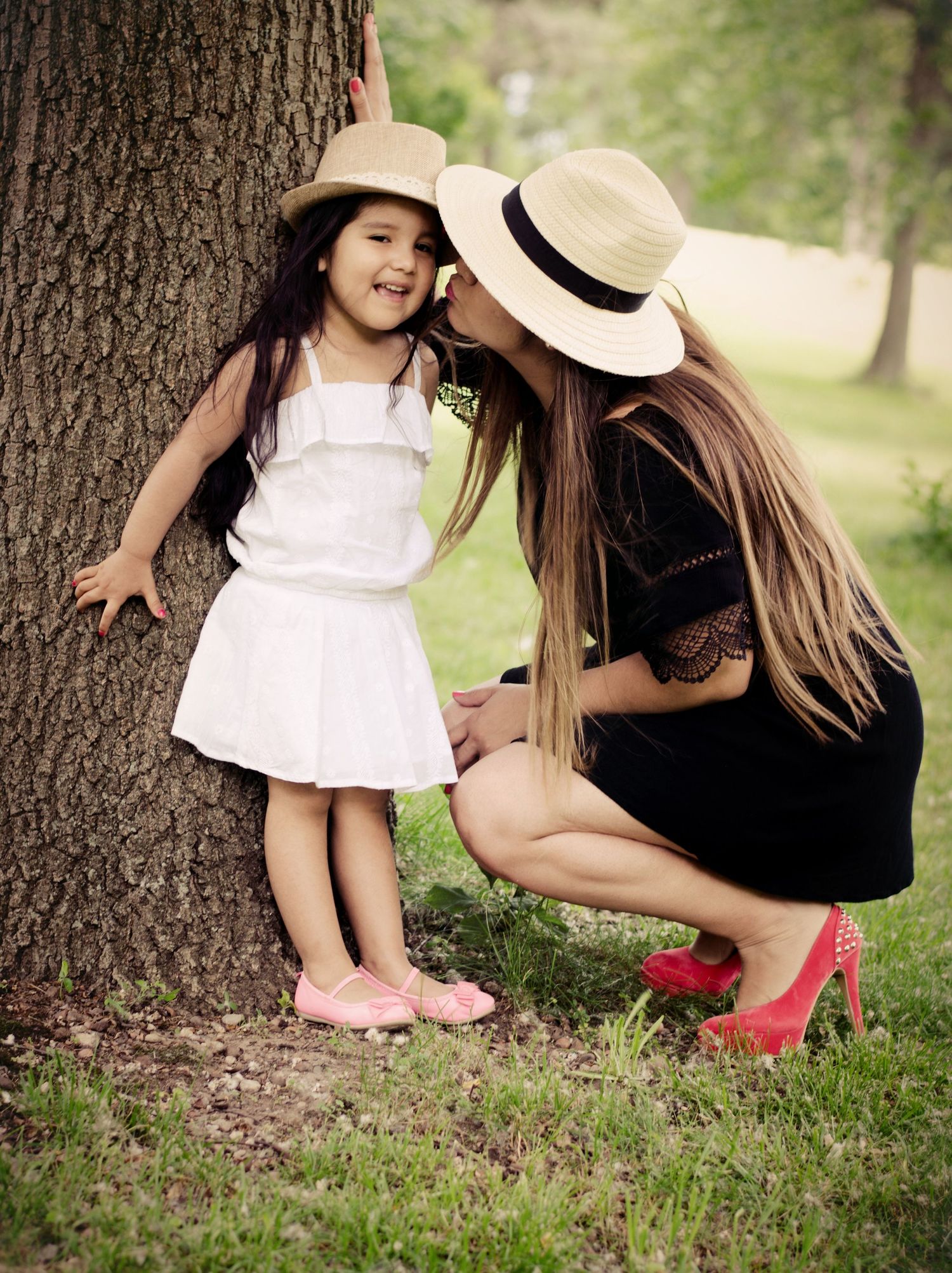 A sweet moment between two people in white and black outfits by a tree trunk.
