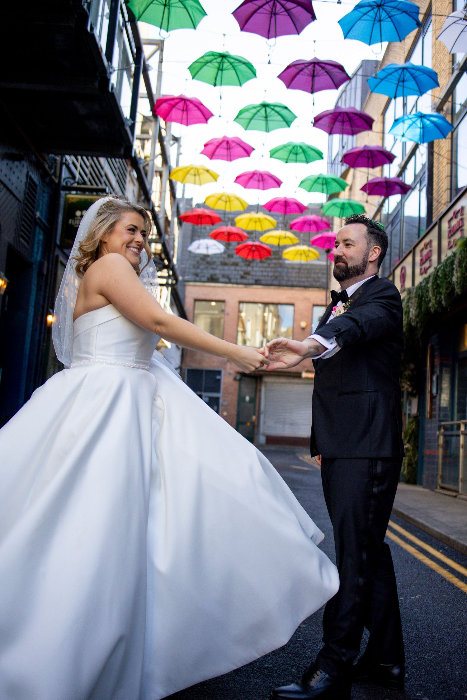 Bride twirls in ballgown under colorful umbrella installation on Dublin street.