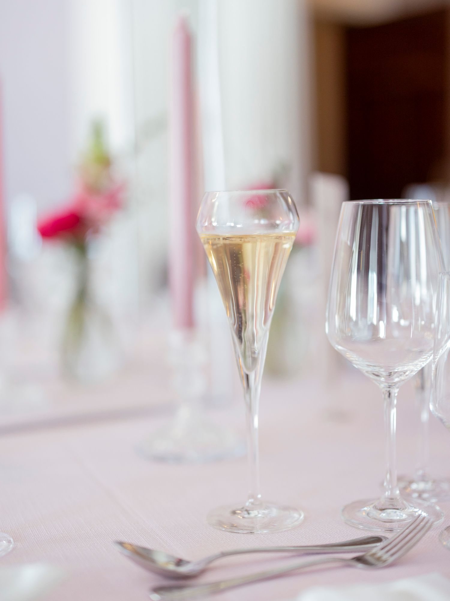 Elegant champagne flute and empty wine glass on a pink tablecloth at a formal event with candles in background.