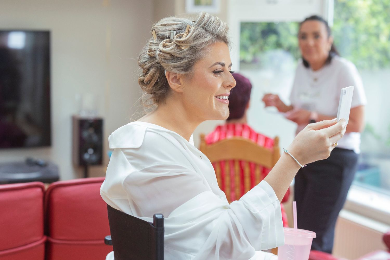 Smiling bride in white robe checking phone during wedding morning preparations at home.