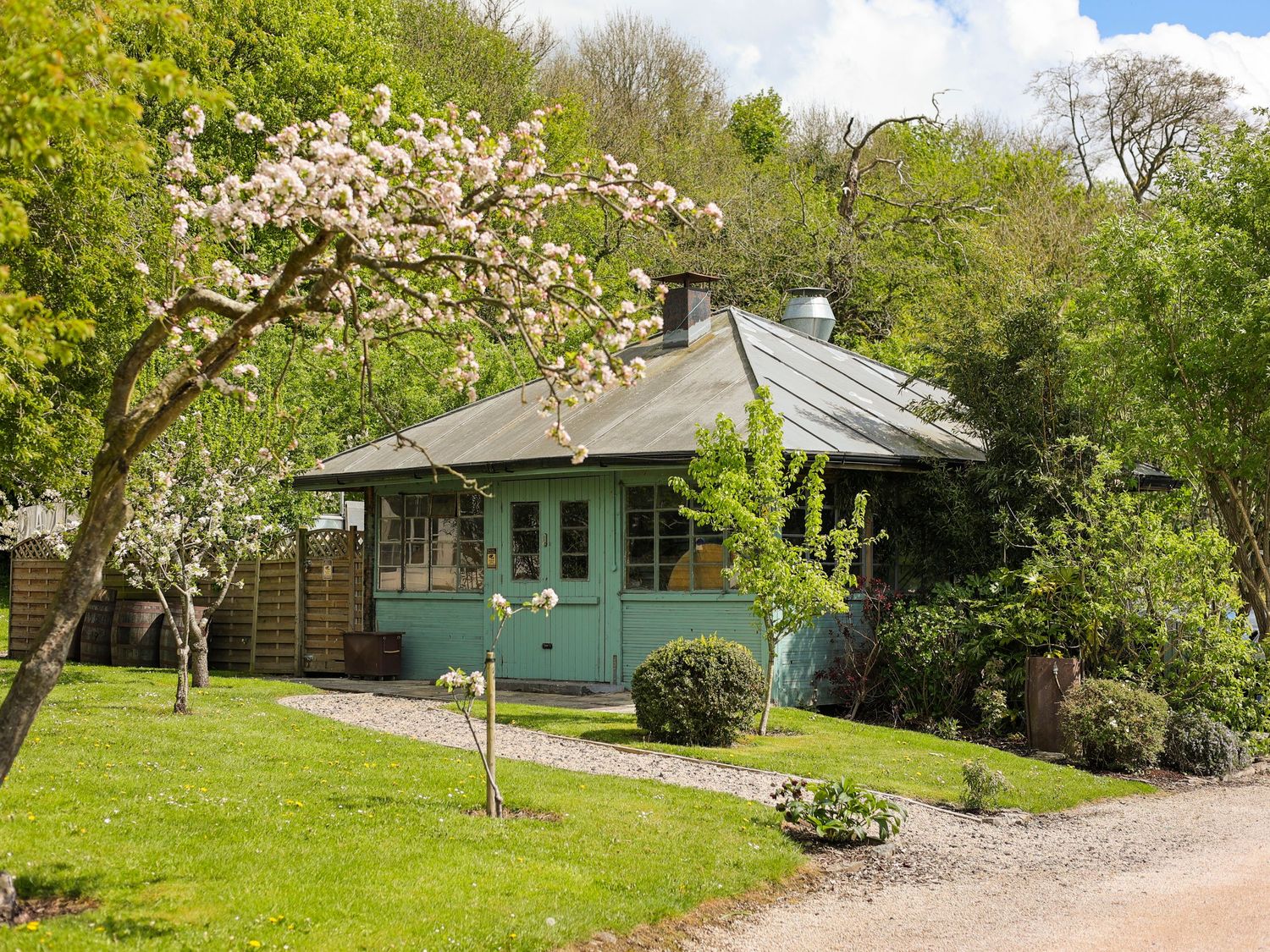 Charming teal wooden cottage surrounded by blossoming trees and lush green lawn on a sunny spring day.