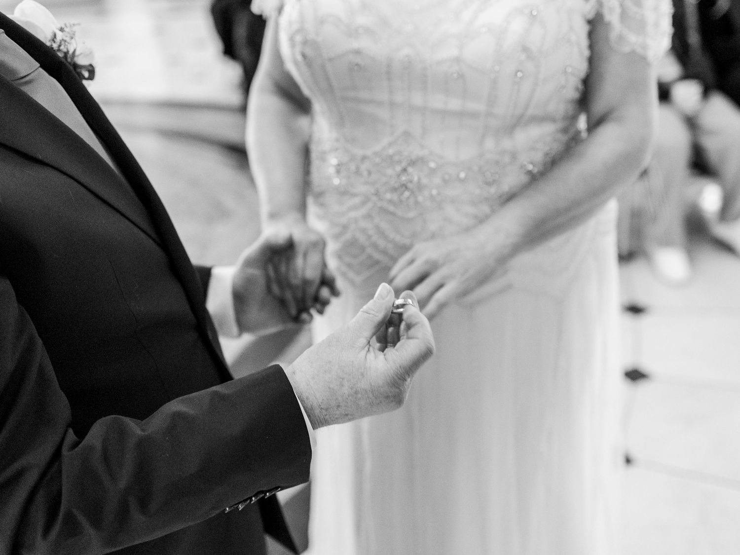 Groom placing wedding ring on brides finger during ceremony in black and white photo.