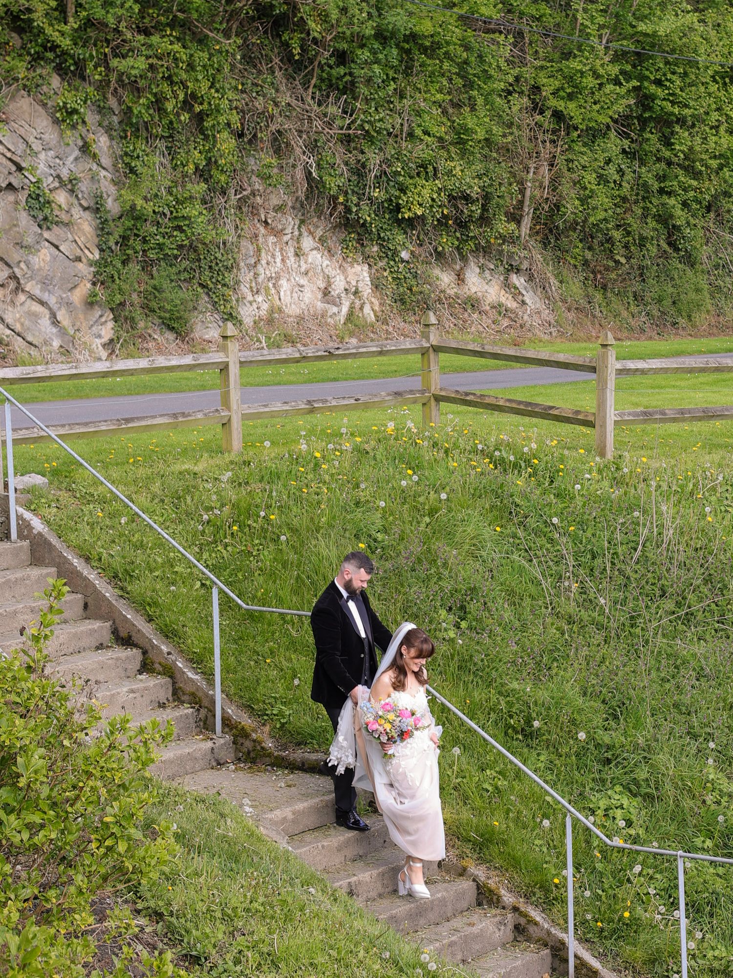 Bride and groom walking up outdoor stone steps surrounded by lush greenery on their wedding day.
