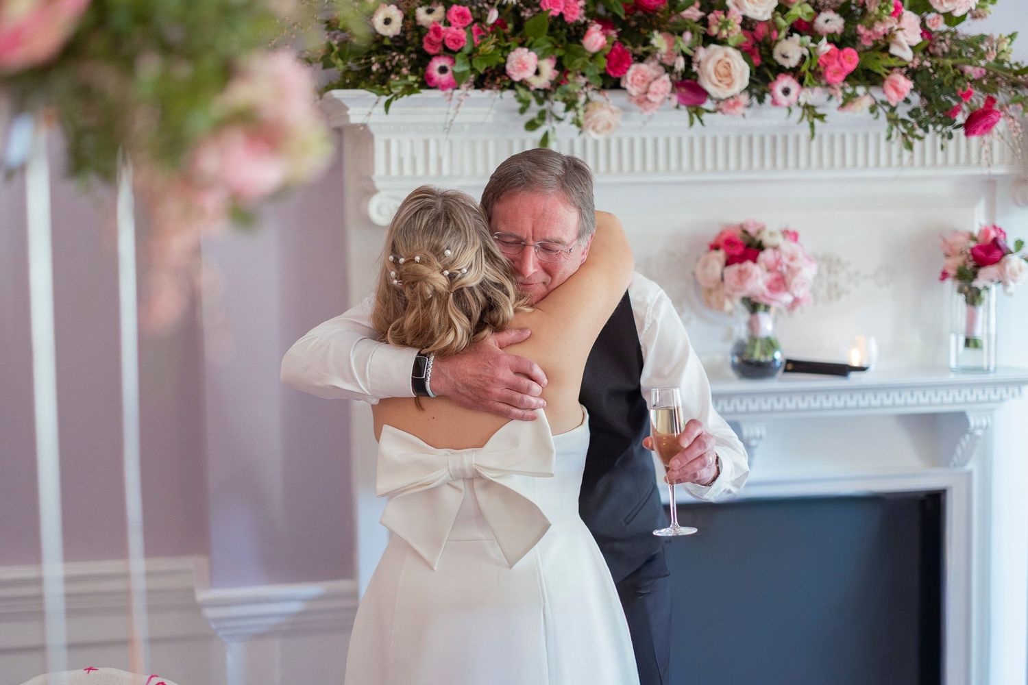 Bride and groom sharing a heartfelt hug near a floral fireplace at their elegant wedding reception.
