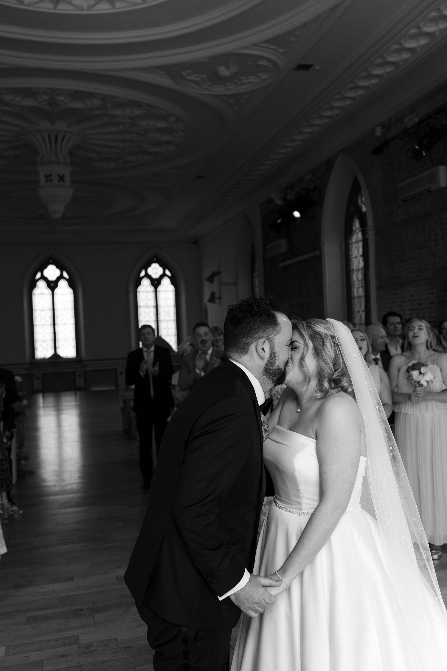 Bride and groom share their first kiss in a stunning black and white photo inside an ornate venue.