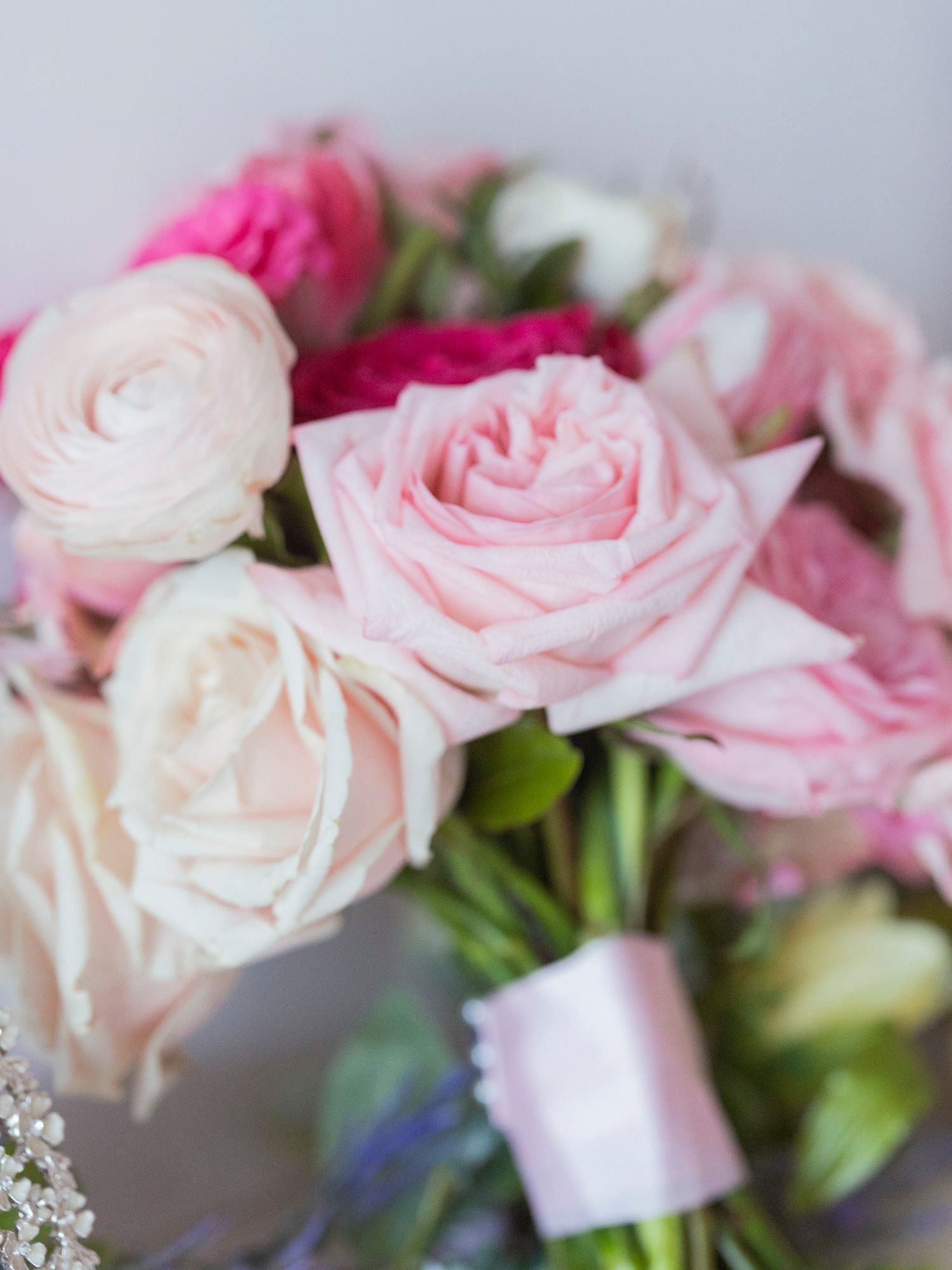 Close-up of a bridal bouquet featuring soft pink roses and ranunculus tied with a pink ribbon.