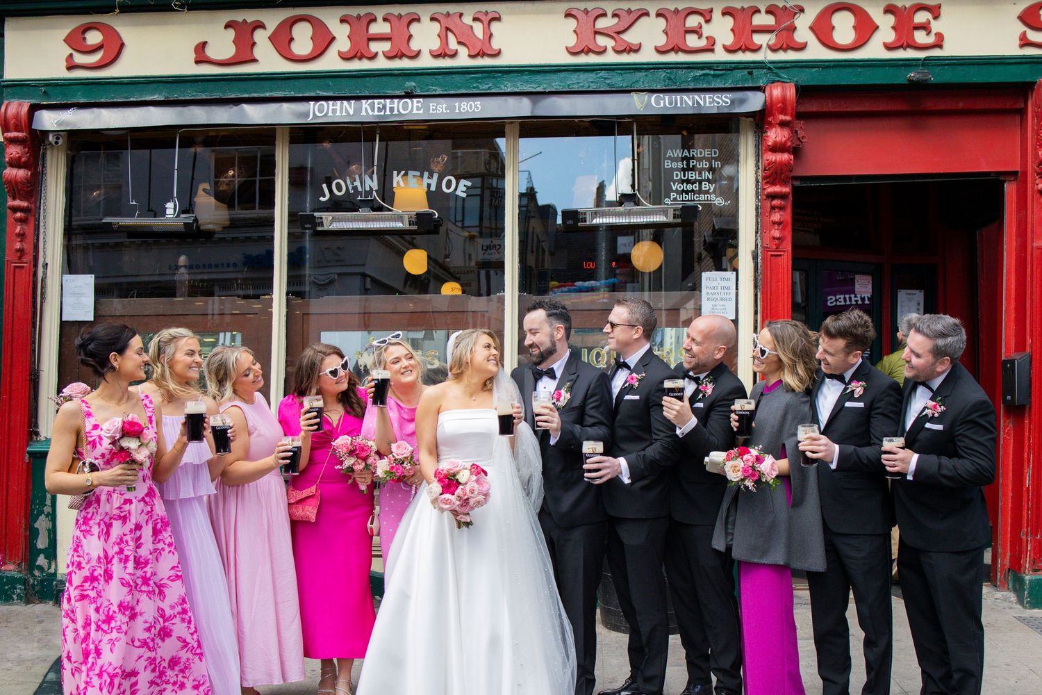 Wedding party poses outside John Kehoe pub in Dublin with bridesmaids in pink dresses.