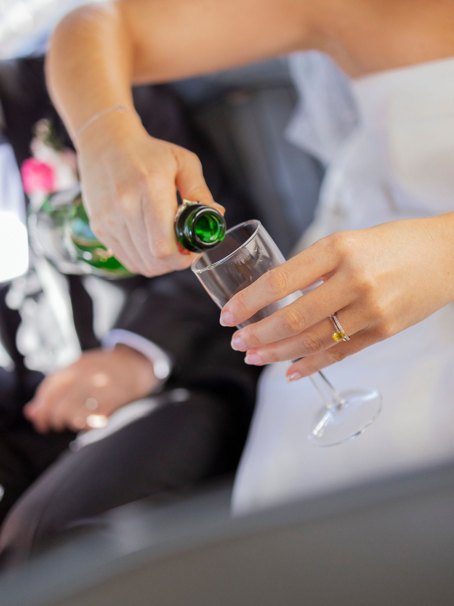 Close-up of bride pouring champagne into a glass while wearing a gold wedding band after ceremony.