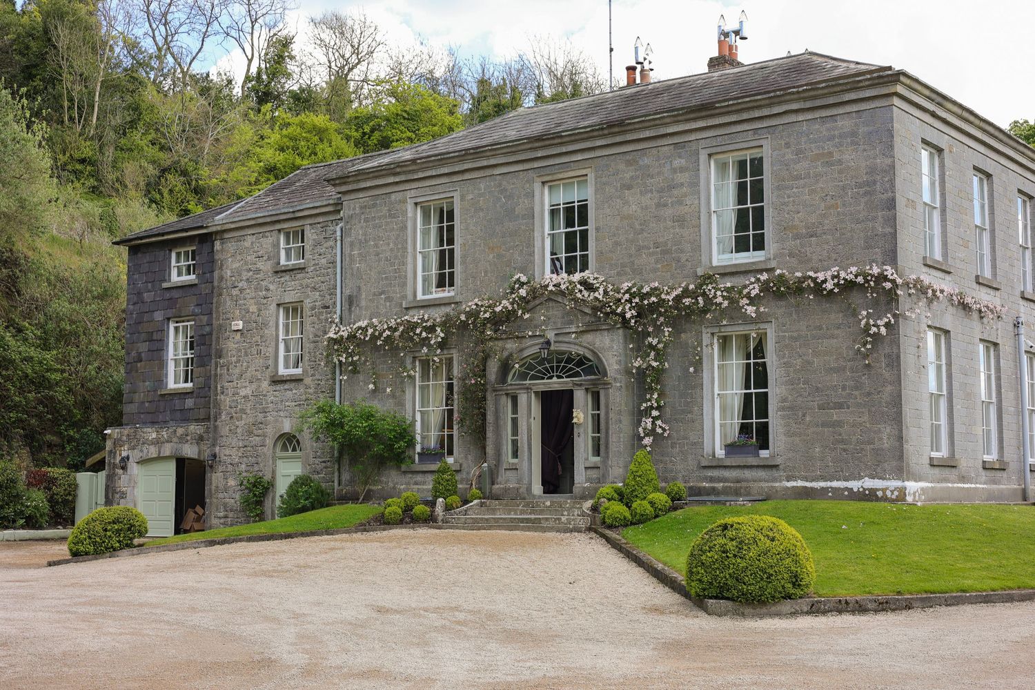 A stunning Georgian stone country house wedding venue with climbing roses and manicured hedges.