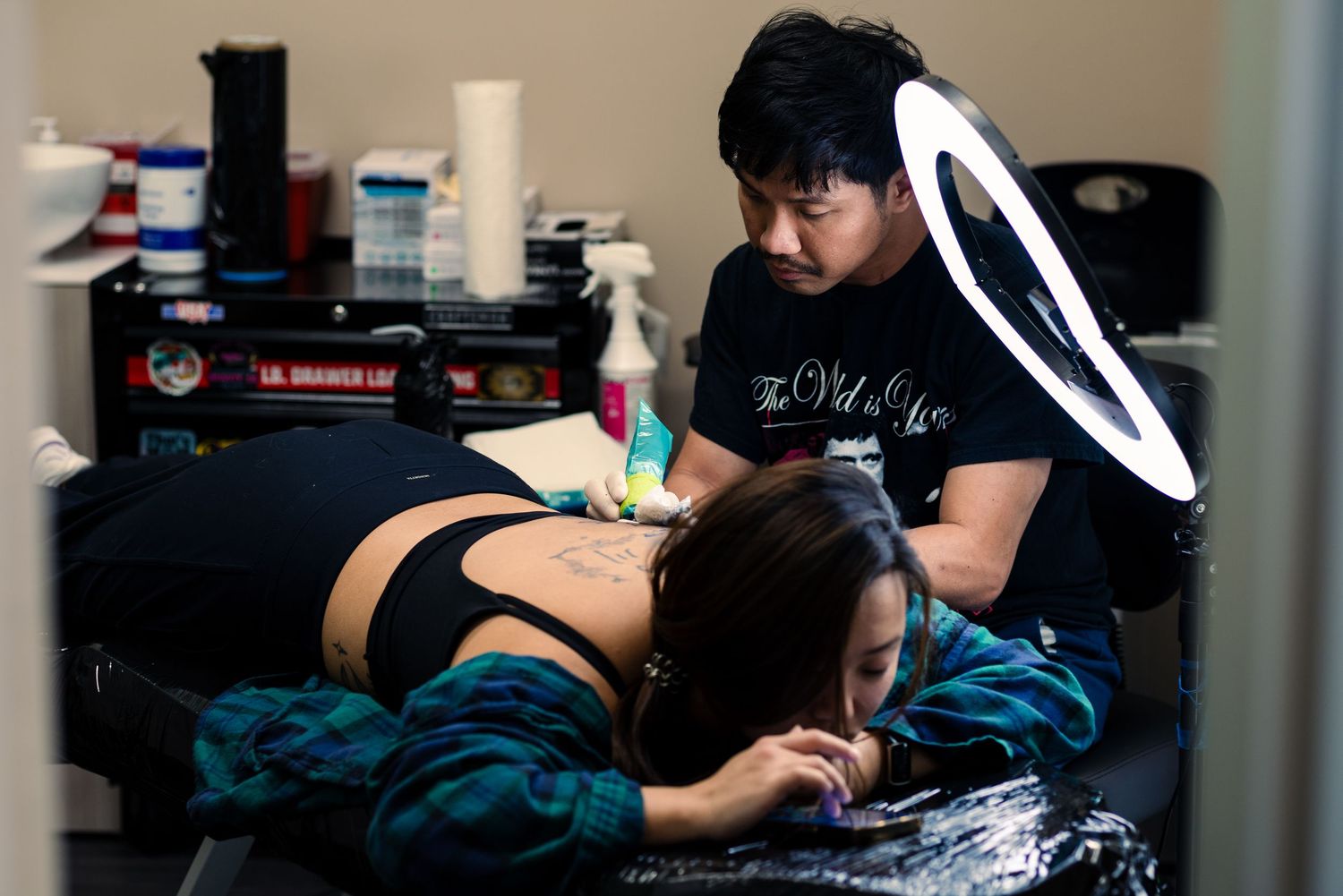 Editorial photograph of a tattoo artist working on a client under ring light — documentary portrait photography by Ground Glass Photography,