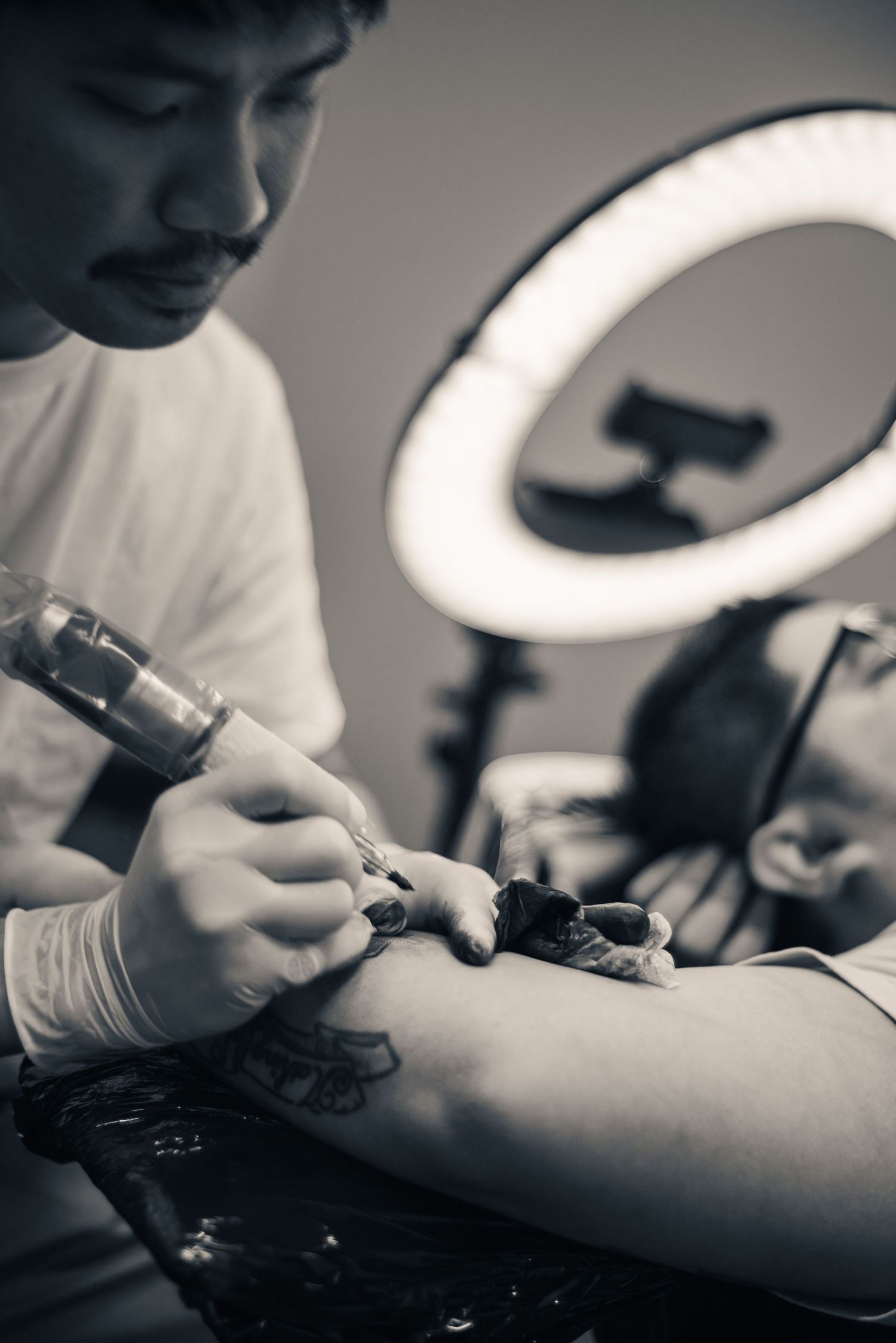 Documentary portrait of a tattoo artist at work under a ring light — editorial photography by Ground Glass Photography, Kent, Washington