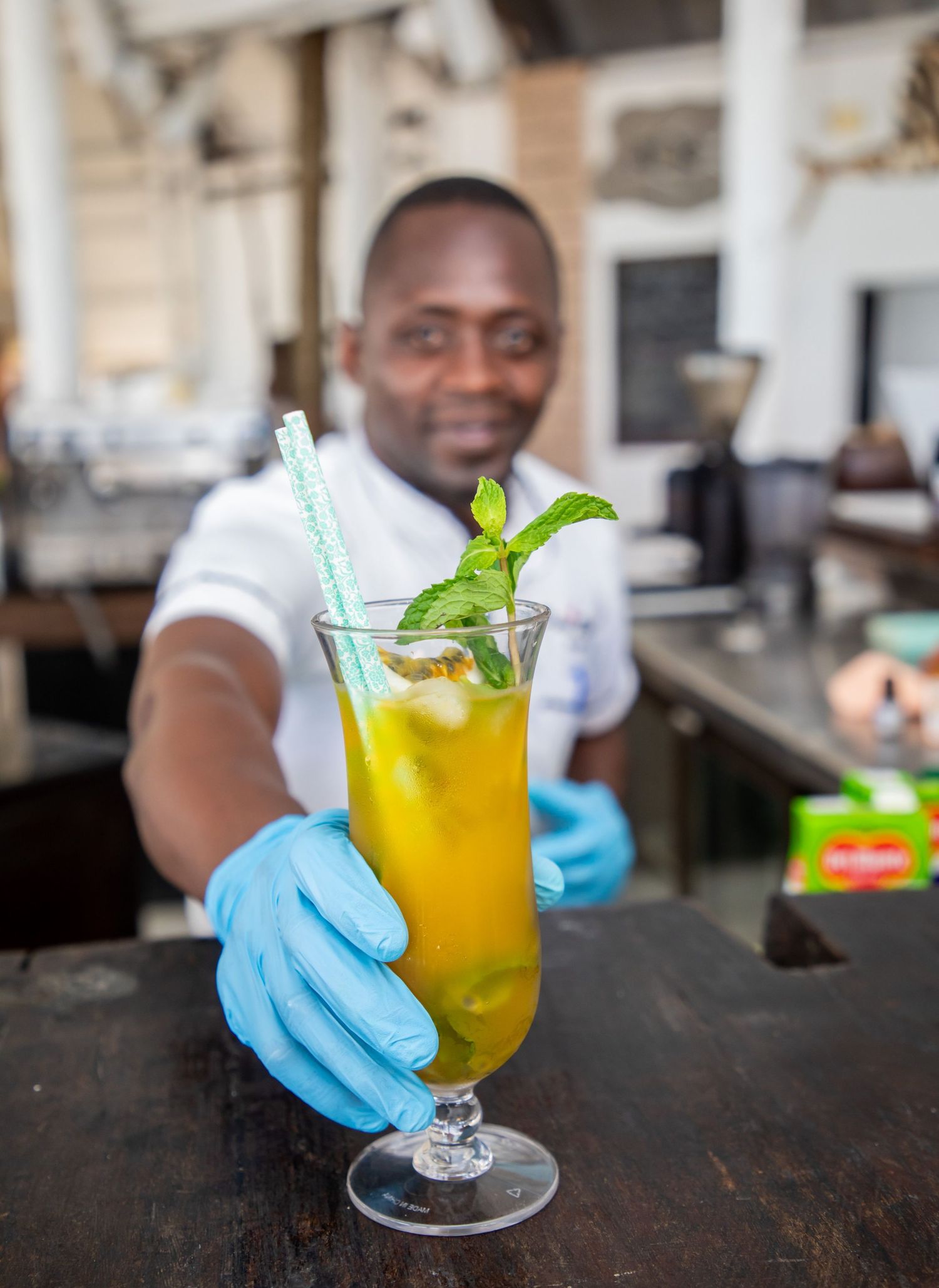 Close-up commercial food and beverage photograph of a yellow iced cocktail garnished with fresh mint leaves and straws.