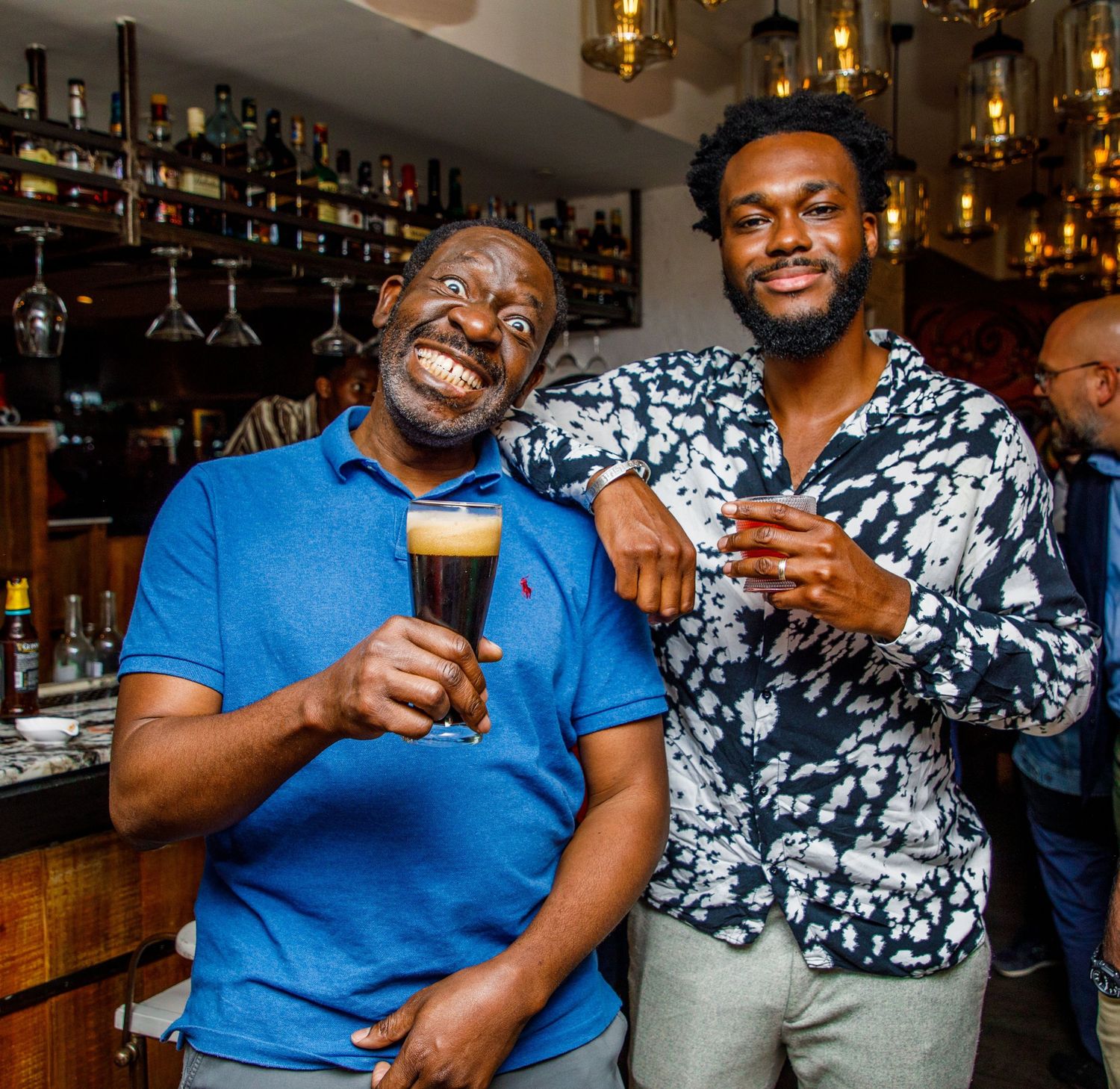 Two men smiling and posing at an indoor bar counter.