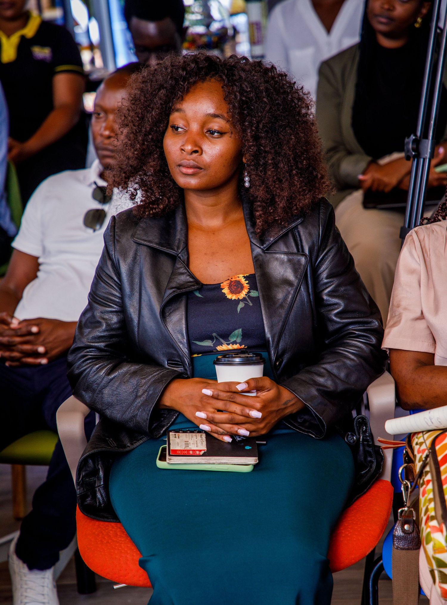 Candid photograph of an attentive woman with curly hair sitting in an audience at a corporate conference or seminar