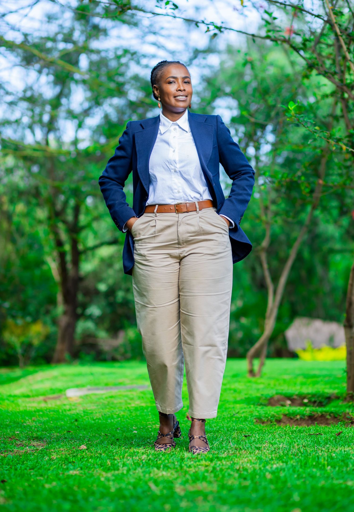 Full-length corporate portrait of a professional woman wearing a navy blue blazer, white shirt, and khaki trousers posing.