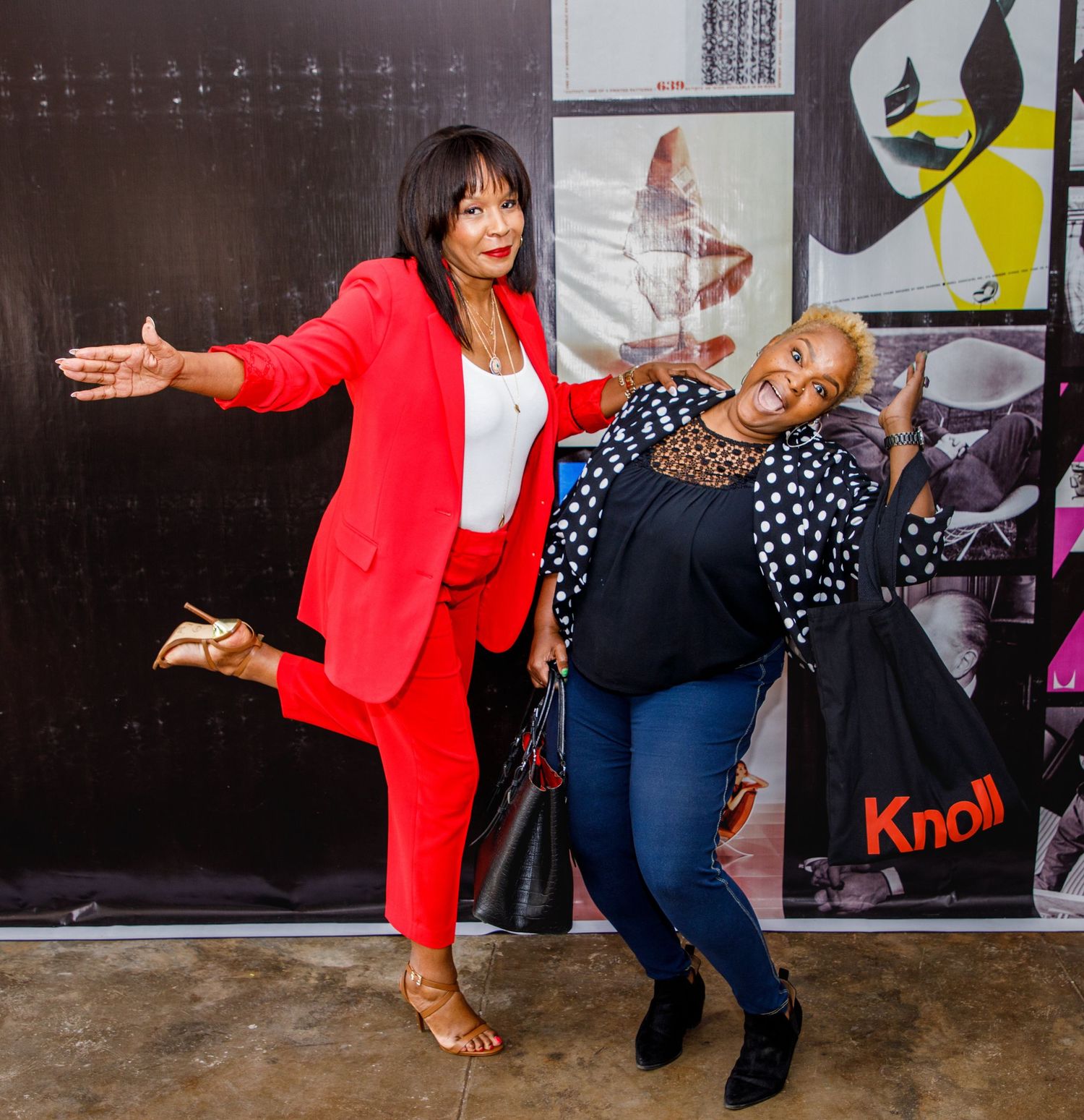 Two smiling women posing playfully together at an indoor corporate event.