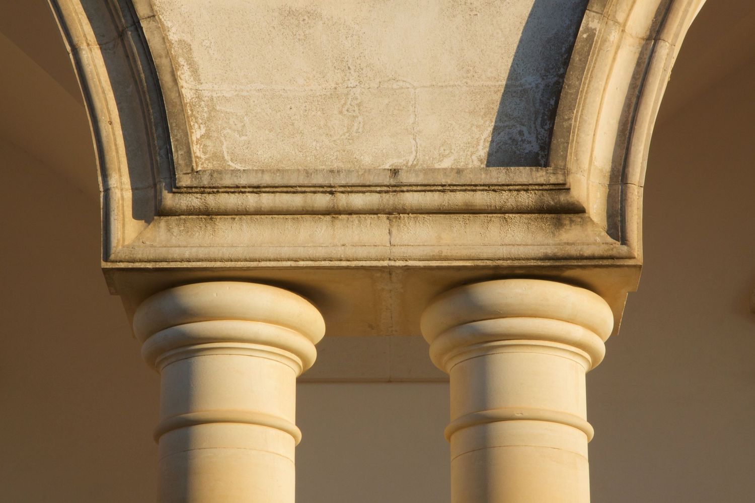Close-up of classical stone columns with ornate capitals supporting an arched portico bathed in warm light.