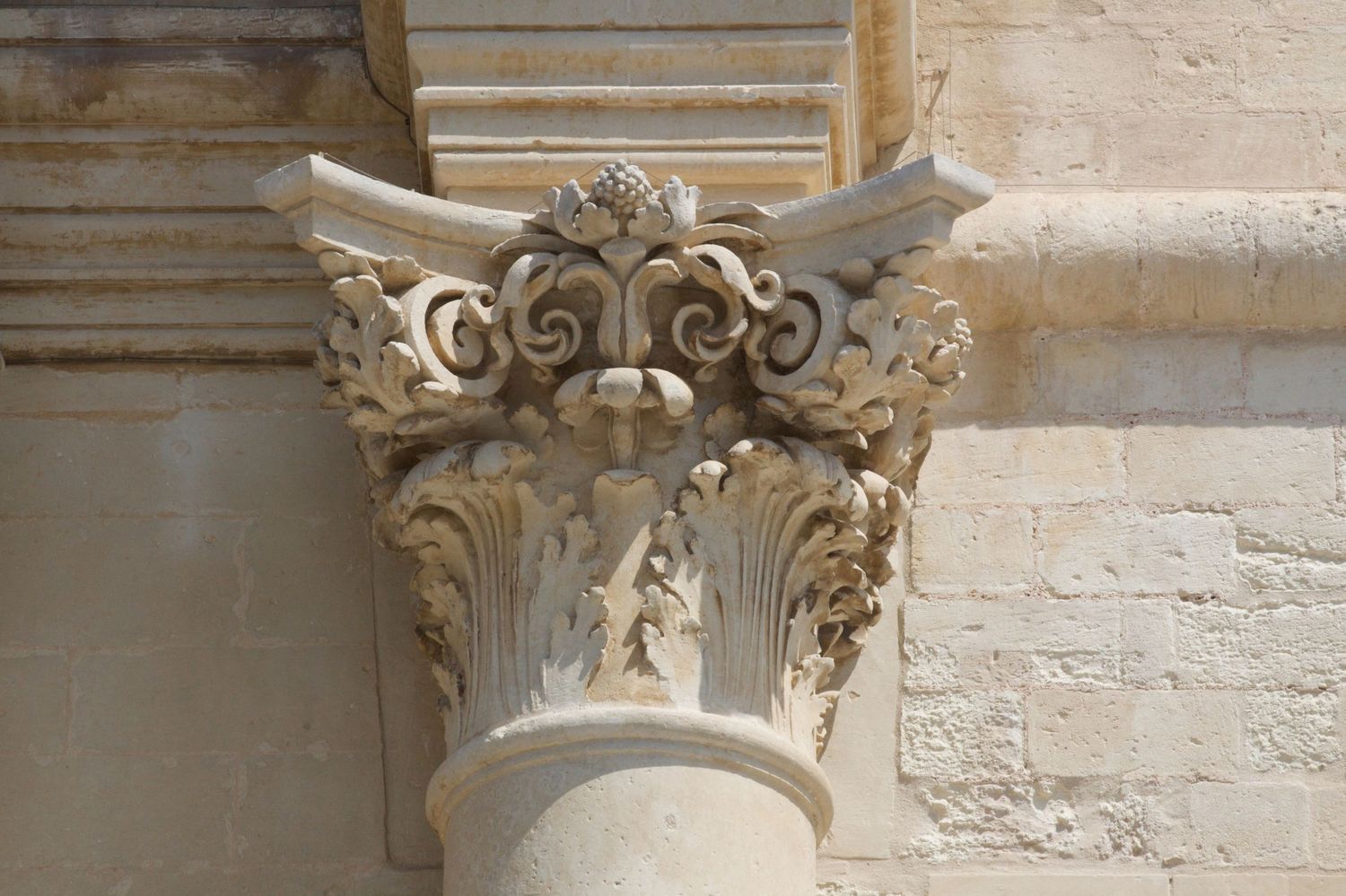 Ornate Baroque stone column capital with intricate carved acanthus leaves and scrollwork details.