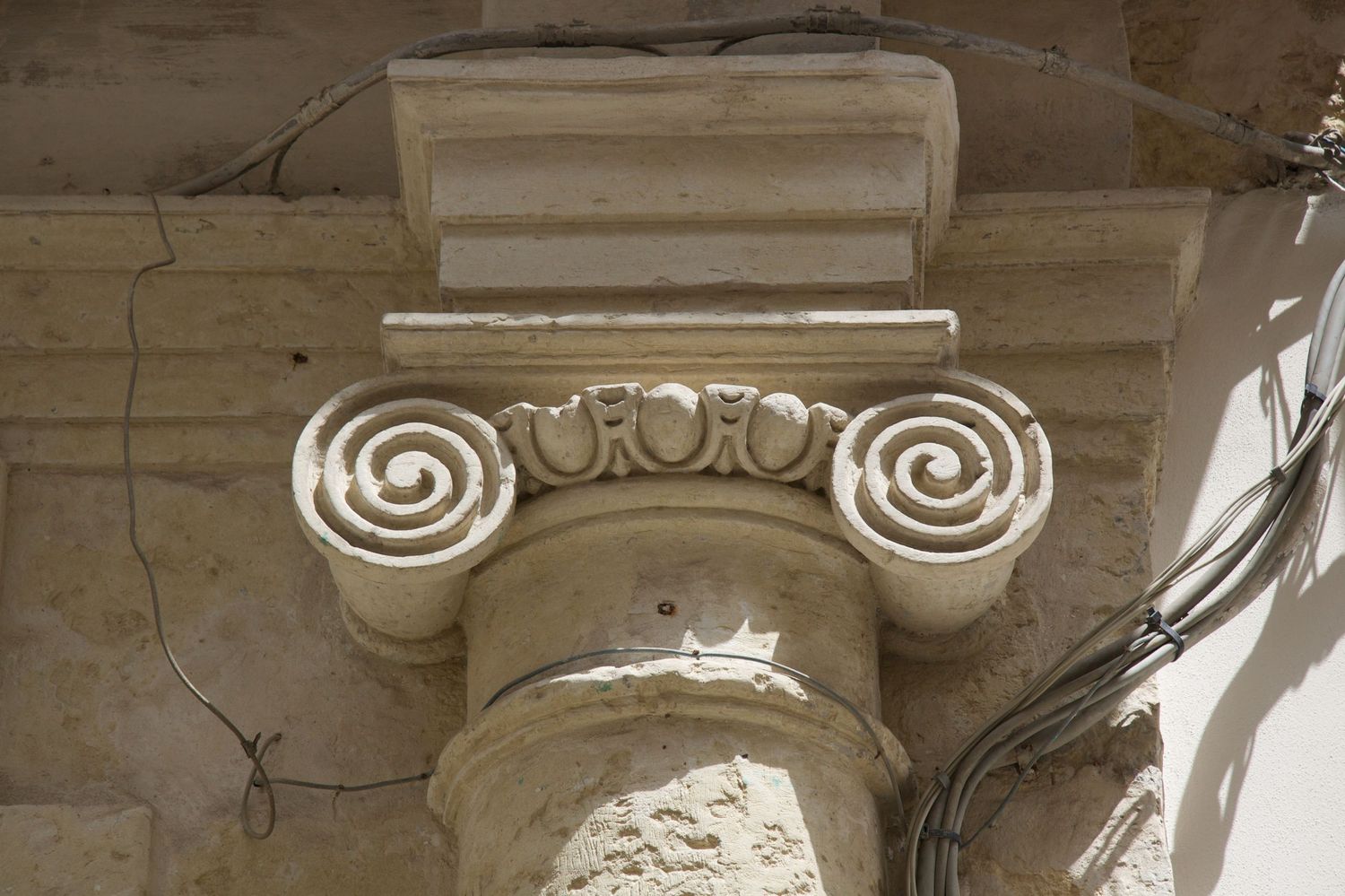 Ancient Ionic column capital with spiral volutes and decorative details on a weathered stone pillar.